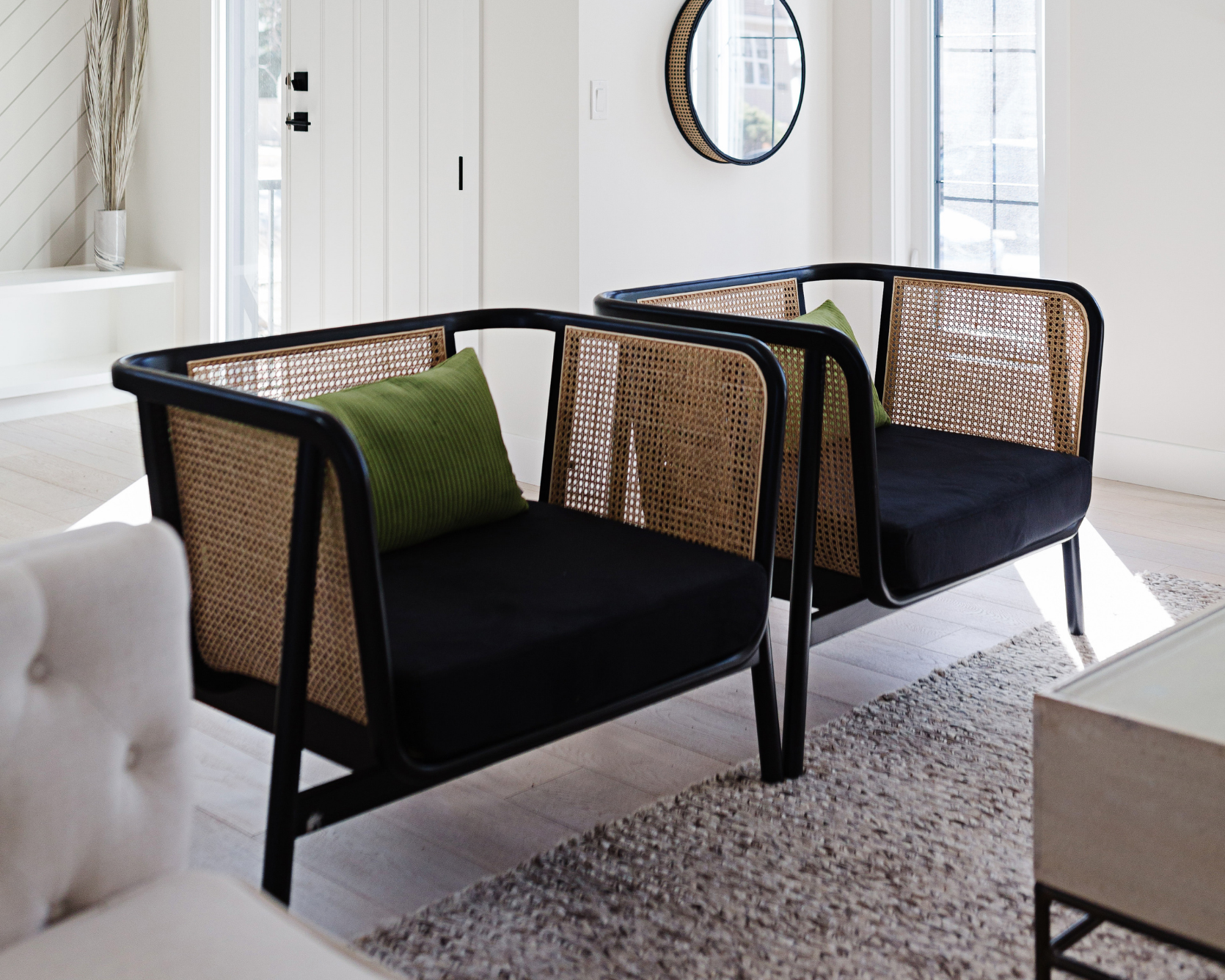 An image of two black and rattan accent chairs with green cushions in a bright minimalist living space with natural light