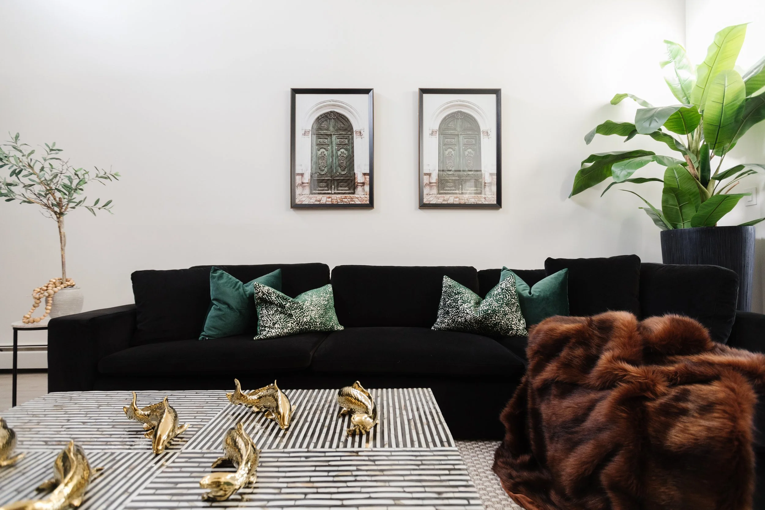 A photo of a modern luxury living room showcasing what is luxury interior design with a black sofa, green accent pillows, and curated wall art.