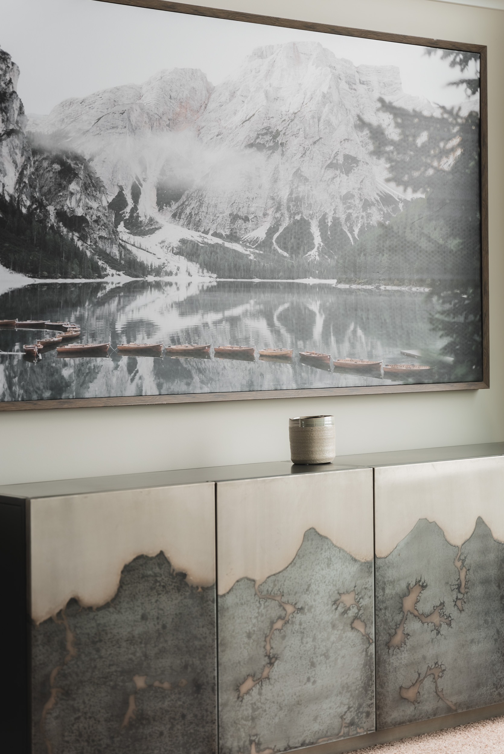 Photo of a modern darkish grey sideboard beneath a framed mountain landscape artwork.