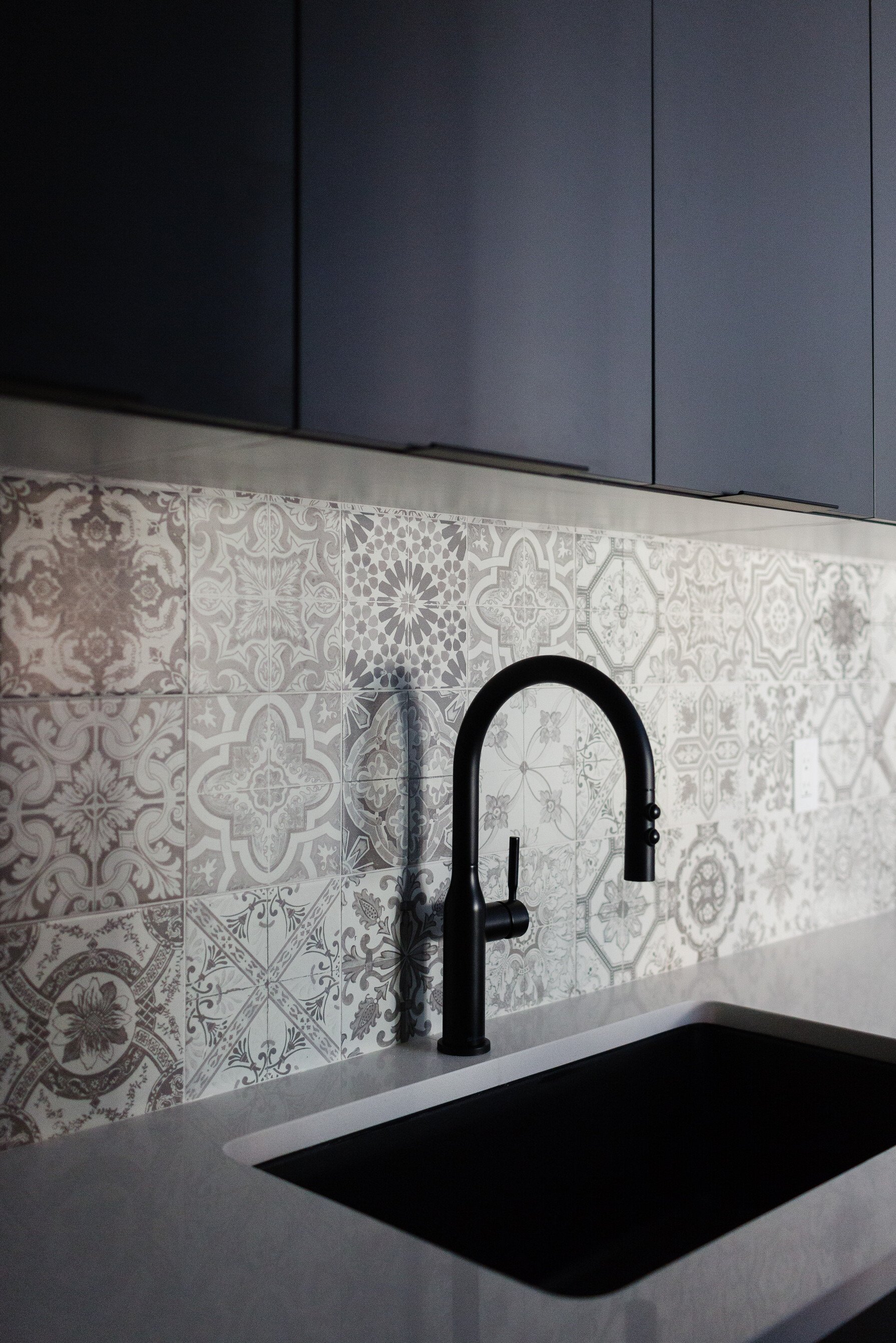 Photo of a handmade vintage grey kitchen backsplash behind a black sink faucet