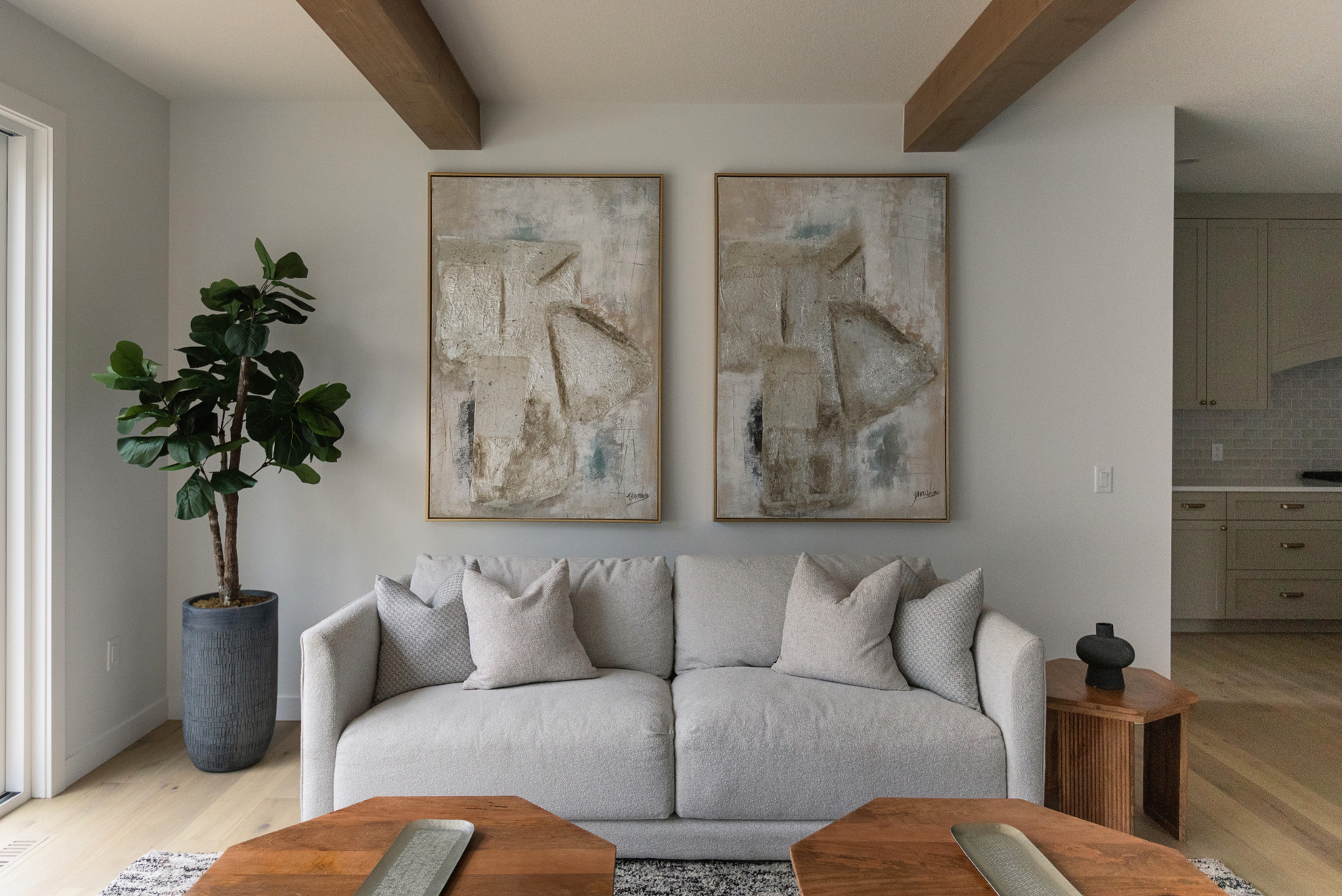Photo of a grey sofa surrounded by a houseplant and wood tables with identical paintings hung above