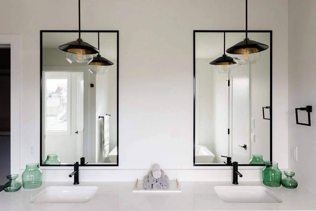Photo of a bathroom vanity with a white countertop, black fixtures, and black-rimmed matching square mirrors with black light fixtures hung above the two sinks