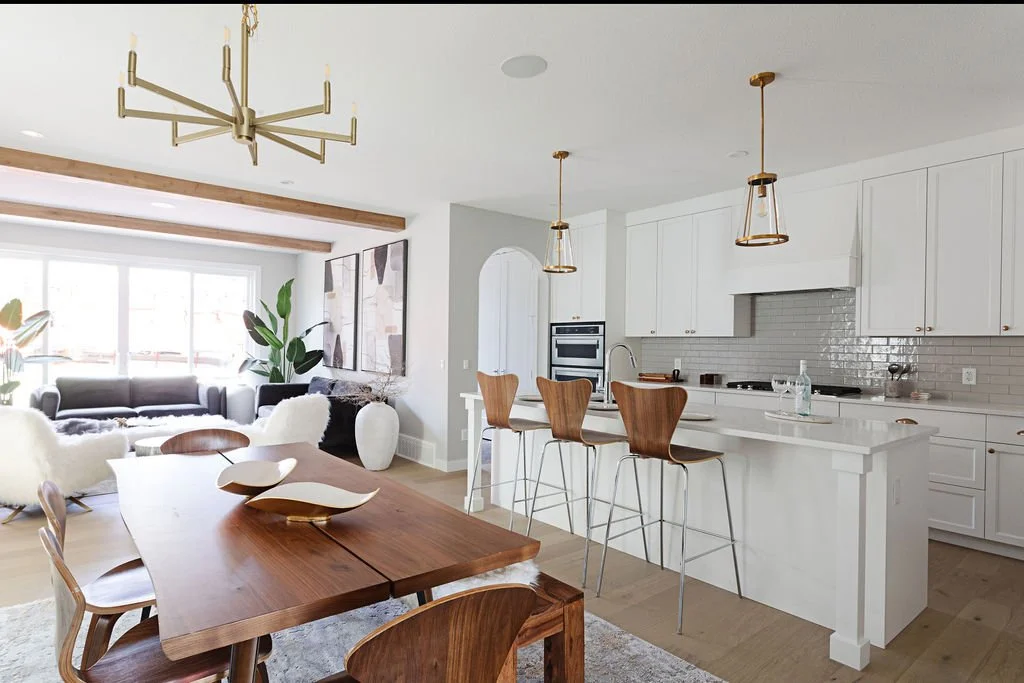 Photo of an open-concept dining room with wood furniture facing a white kitchen with a large white island, wood chairs and a living room in the background