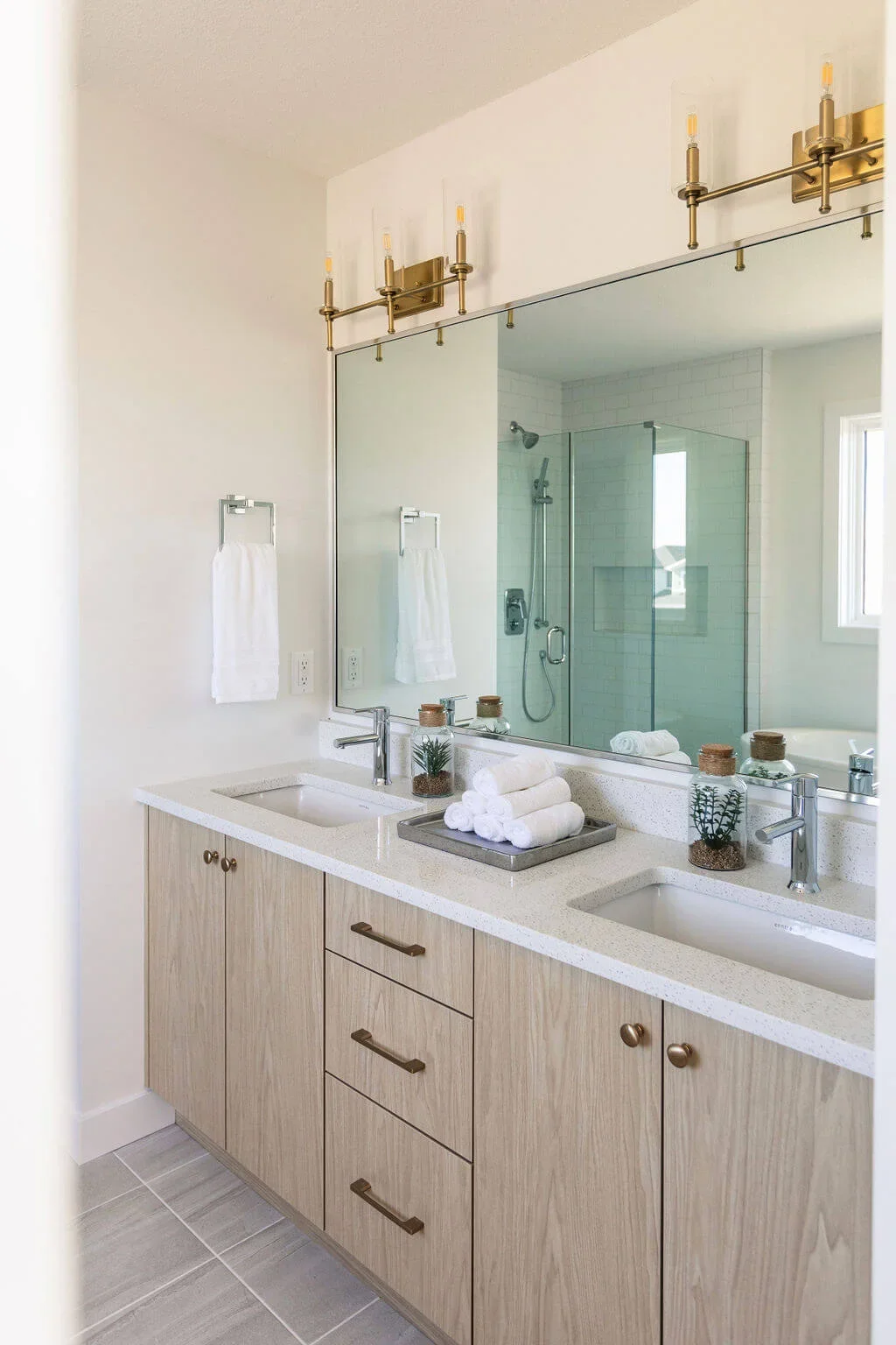 photo of a bathroom vanity with wood cabinets a white granite countertop and two sinks with a large mirror and gold light fixtures
