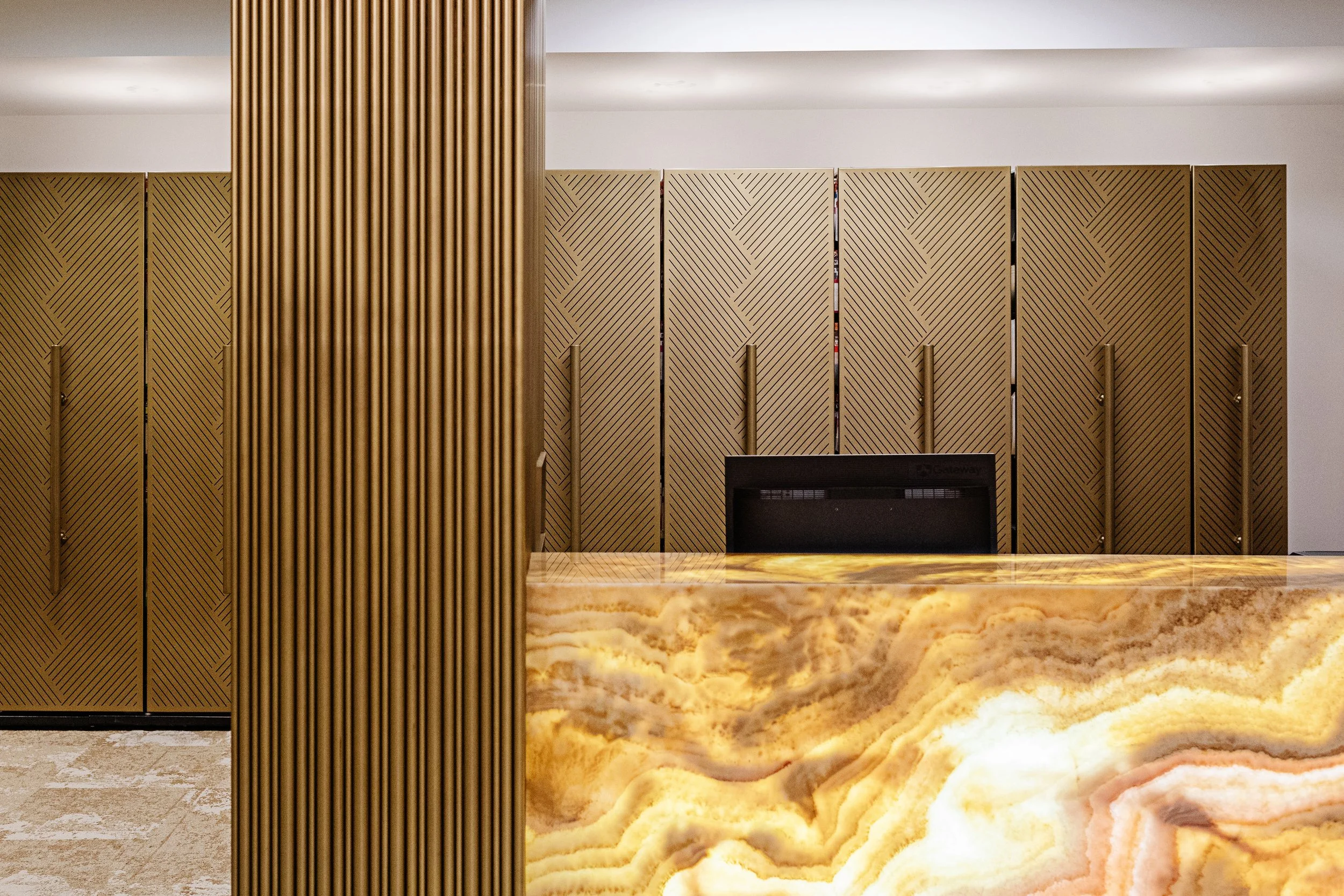 Picture of a sleek line of gold cupboards framed by a gridded gold feature wall and a richly veined gold marble surface