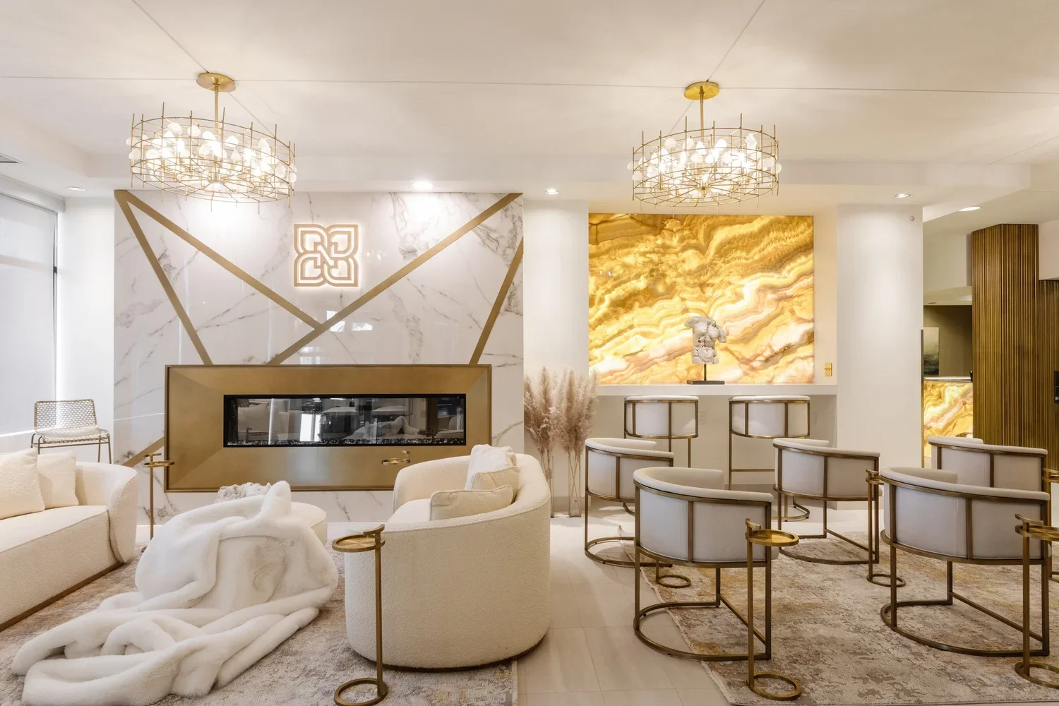 photo of a waiting room with white sofas and chairs, gold and white marble walls, and gold chandeliers