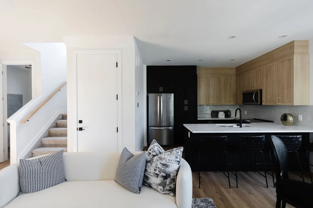 Picture of an open-concept basement living area with a white curved sofa, a black kitchen island, and light wood cabinetry