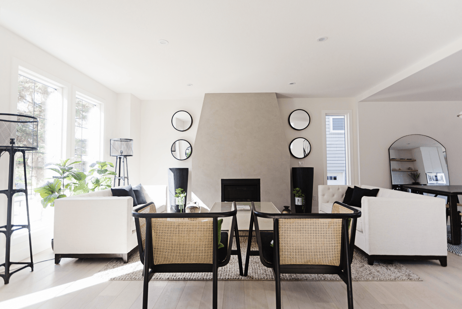 Photo of how to design a contemporary home showing the back of two bamboo chairs in a modern white living room facing a fireplace and two white sofas surronded by mirrors