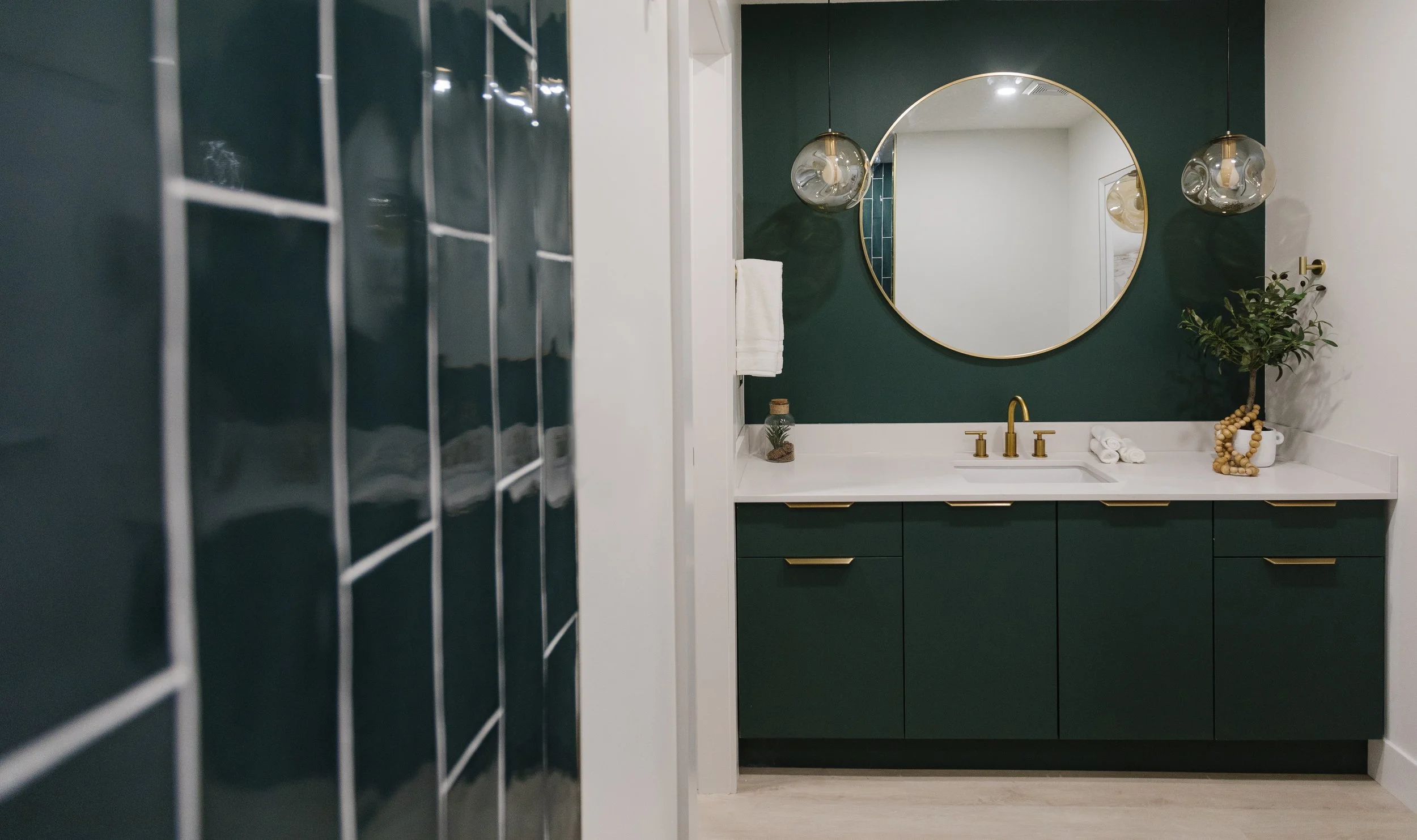Photo of a bathroom with turquoise countertop and walls, with gold fixtures, and a gold rimming round vanity mirror above a sink