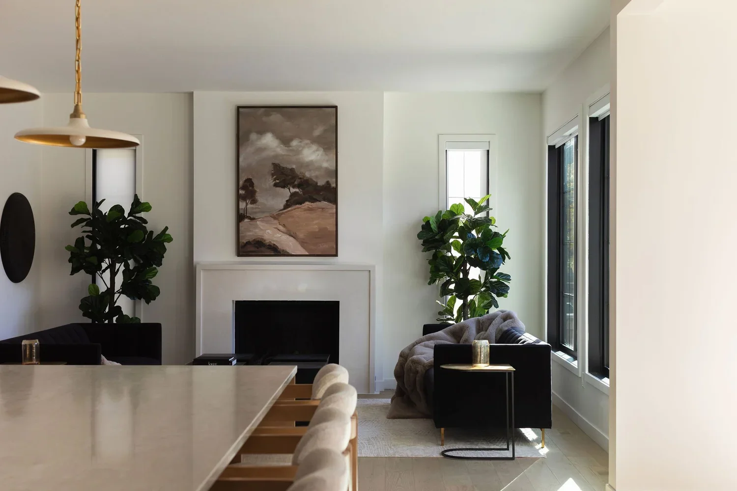 photo of a living room and kitchen with a fireplace artwork plants and black sofas with a brown granite kitchen island in the forefront