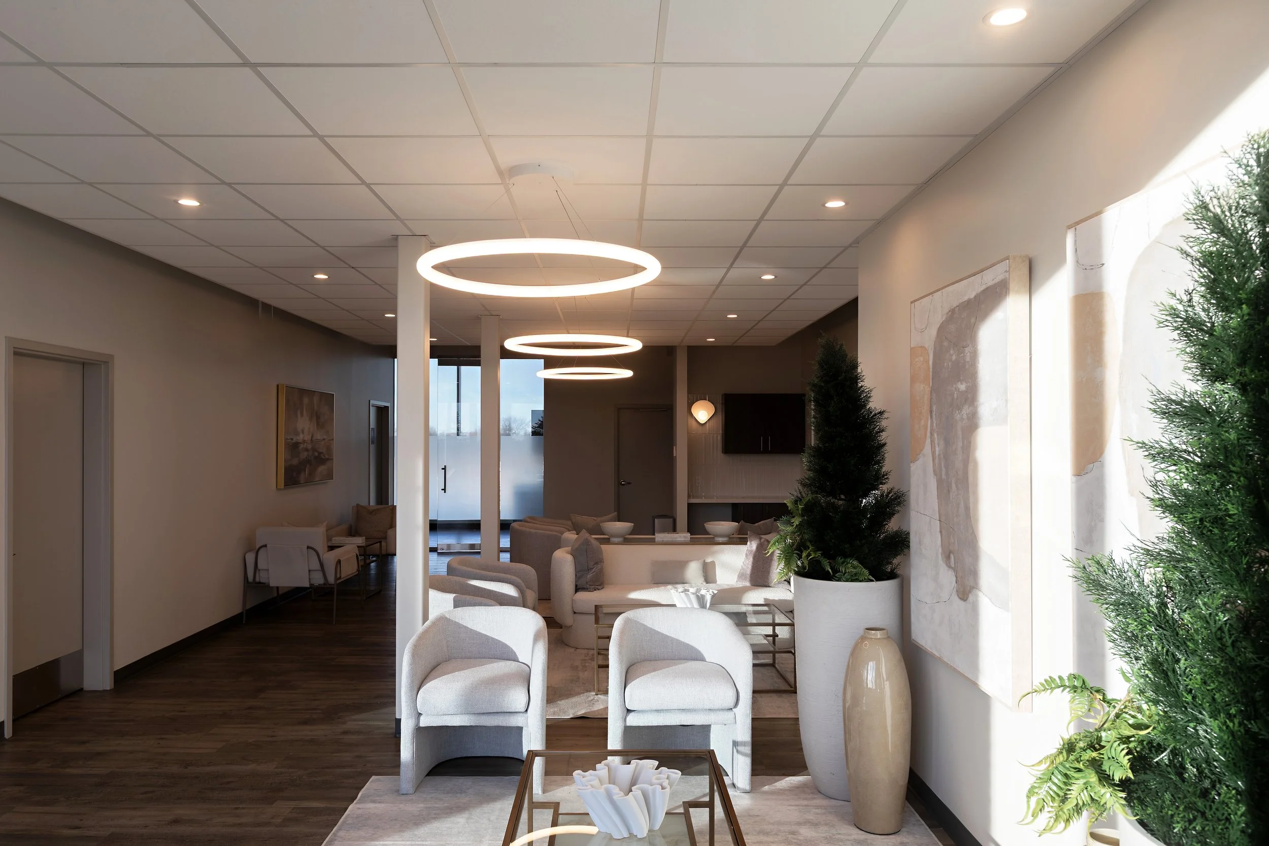 Photo of a waiting room with grey armchairs, white sofas, modern decor, and circular light fixtures above
