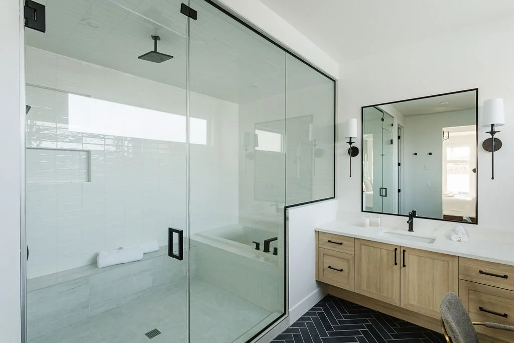 Photo of a stand-up shower and wood vanity with black fixtures and black rims around the mirror and shower wall accenting, a wood vanity, and black tiled flooring