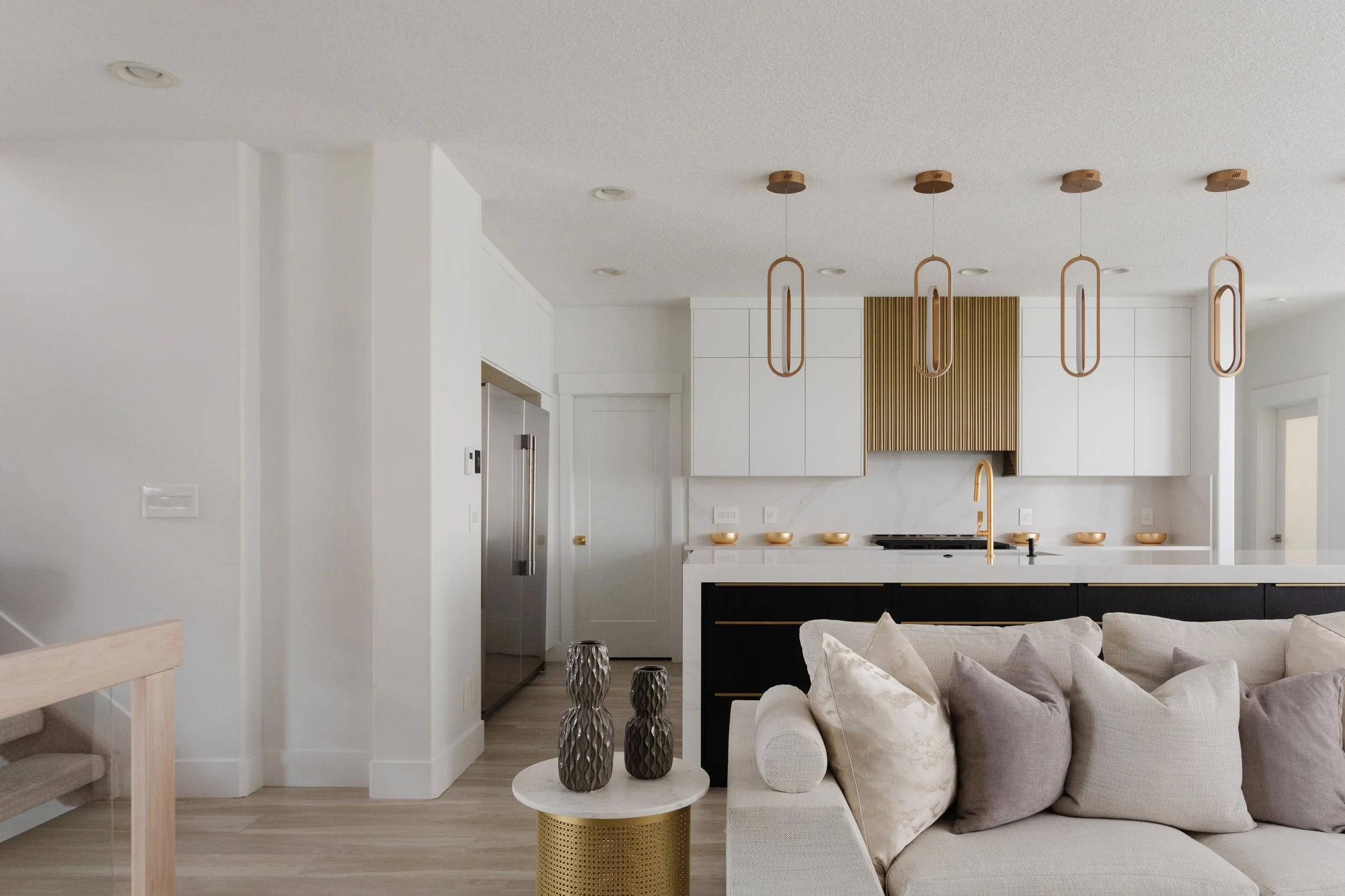 Photo of a white modern kitchen with white countertops and gold decor and a white couch with pillows in forefront for what is turnkey projects