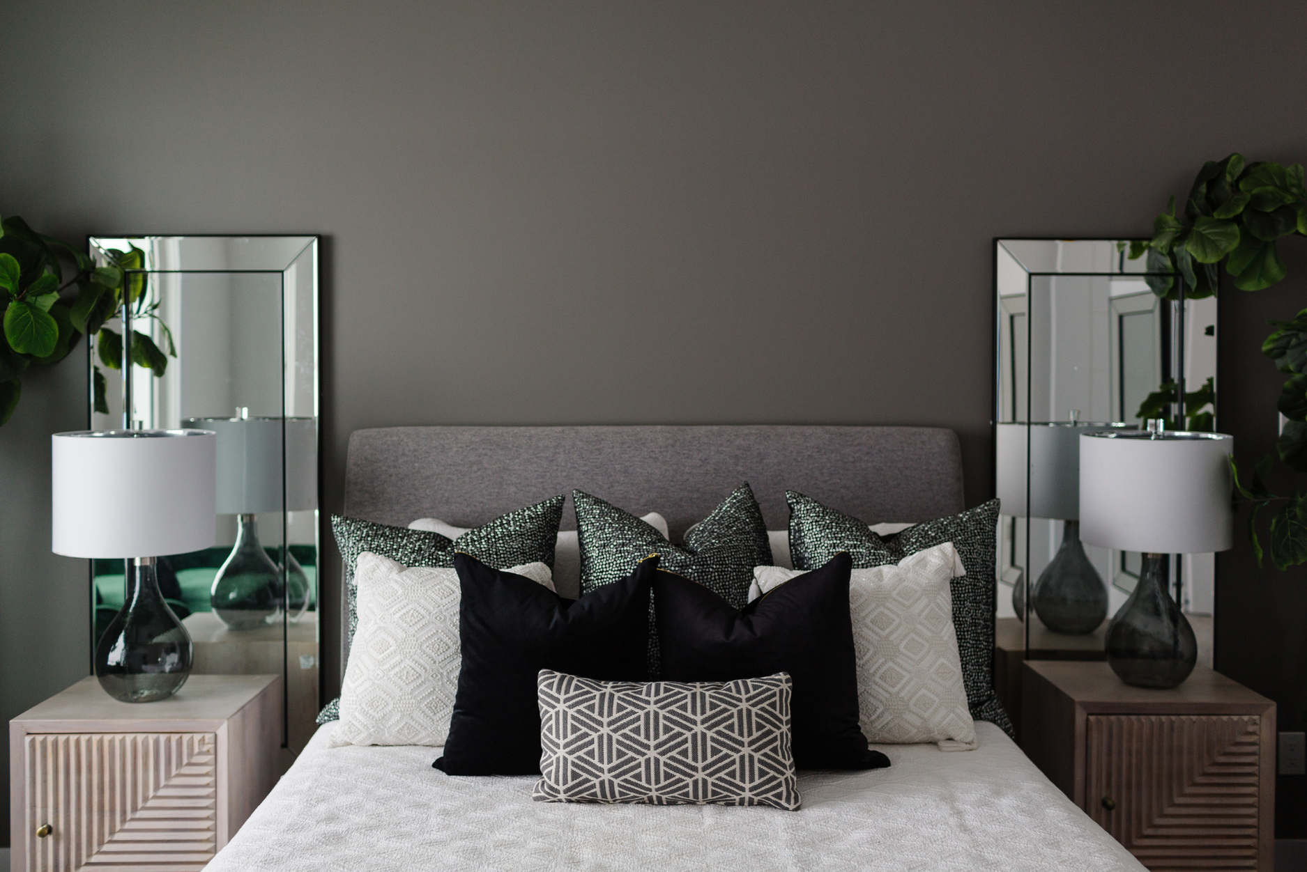 A photo of a luxurious bedroom with layered bedding, mirrors behind matching nightstands, and soft lighting.