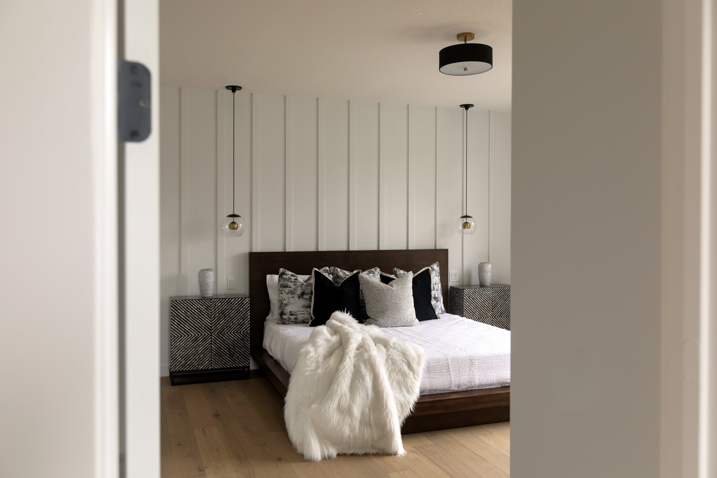 Photo of a bedroom door open with white queen-sized bed and fur blanket