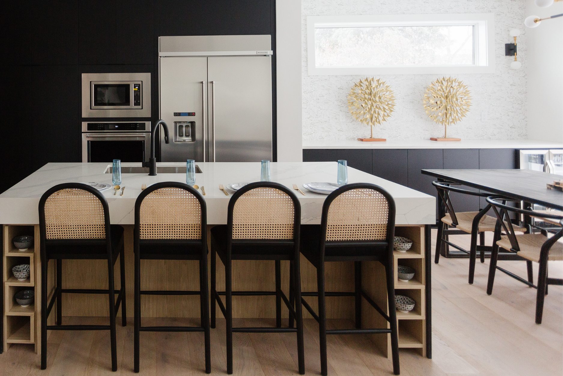 Photo of a Japanese interior design kitchen with a large whie marble island and chairs facing stainless steel appliances integrated into black cabinets