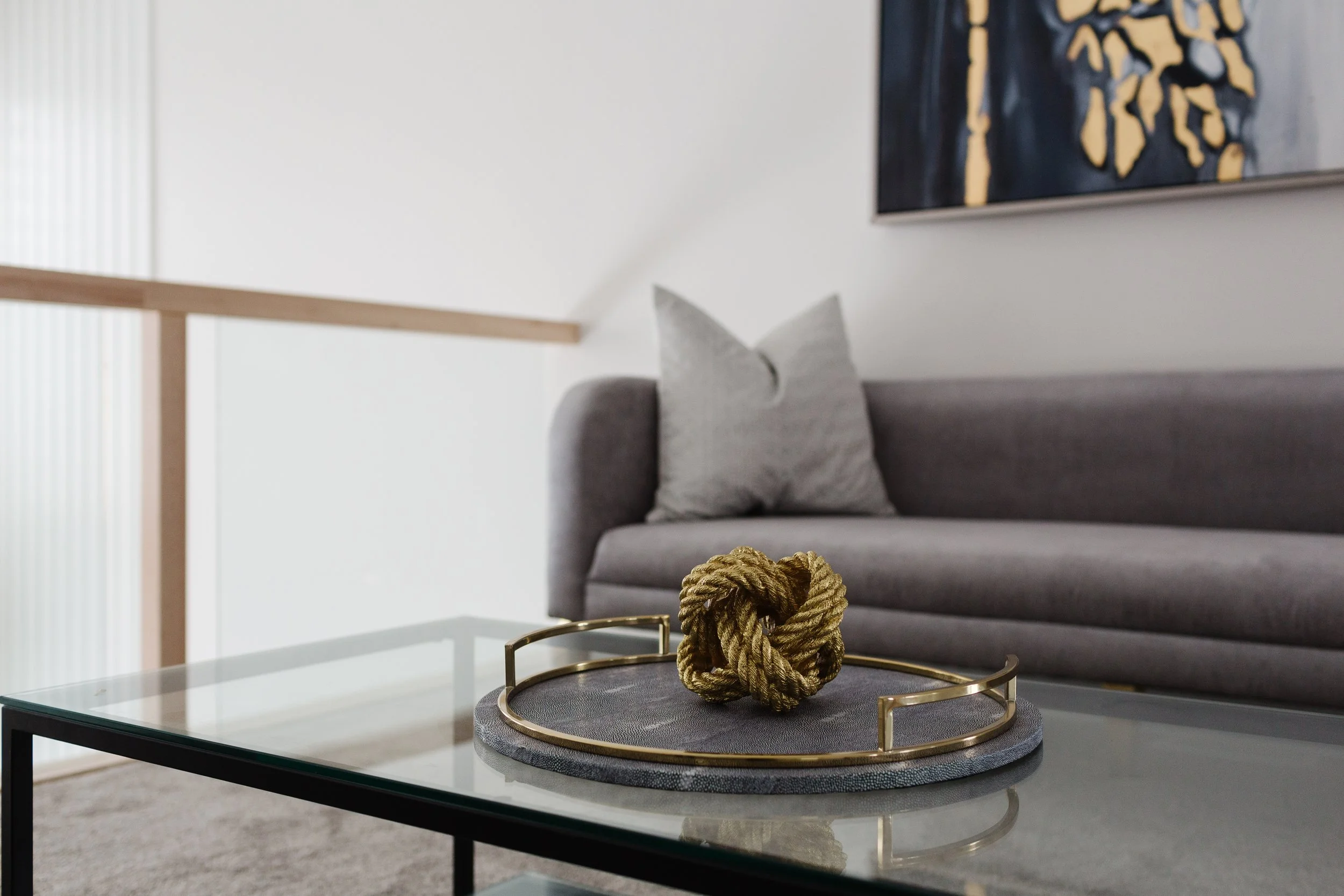 Photo of gold decor in a grey and gold tray on a glass coffee table in front of a grey sofa