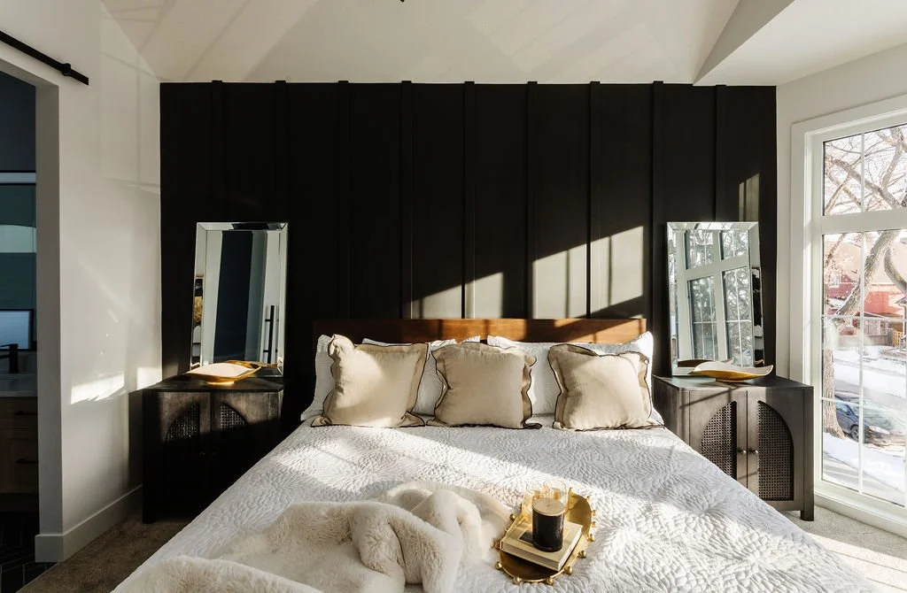Photo of a black feature wall in a bedroombehind a white queen-sized bed with two mirrors and matching nightstands on either side and blankets, a tray, and throw pillows on the bed
