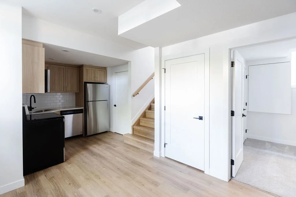 Picture of a modern basement entryway and kitchenette done with simple finished basement ideas, featuring light wood luxury vinyl plank flooring, white shaker style doors, and a stainless steel refrigerator