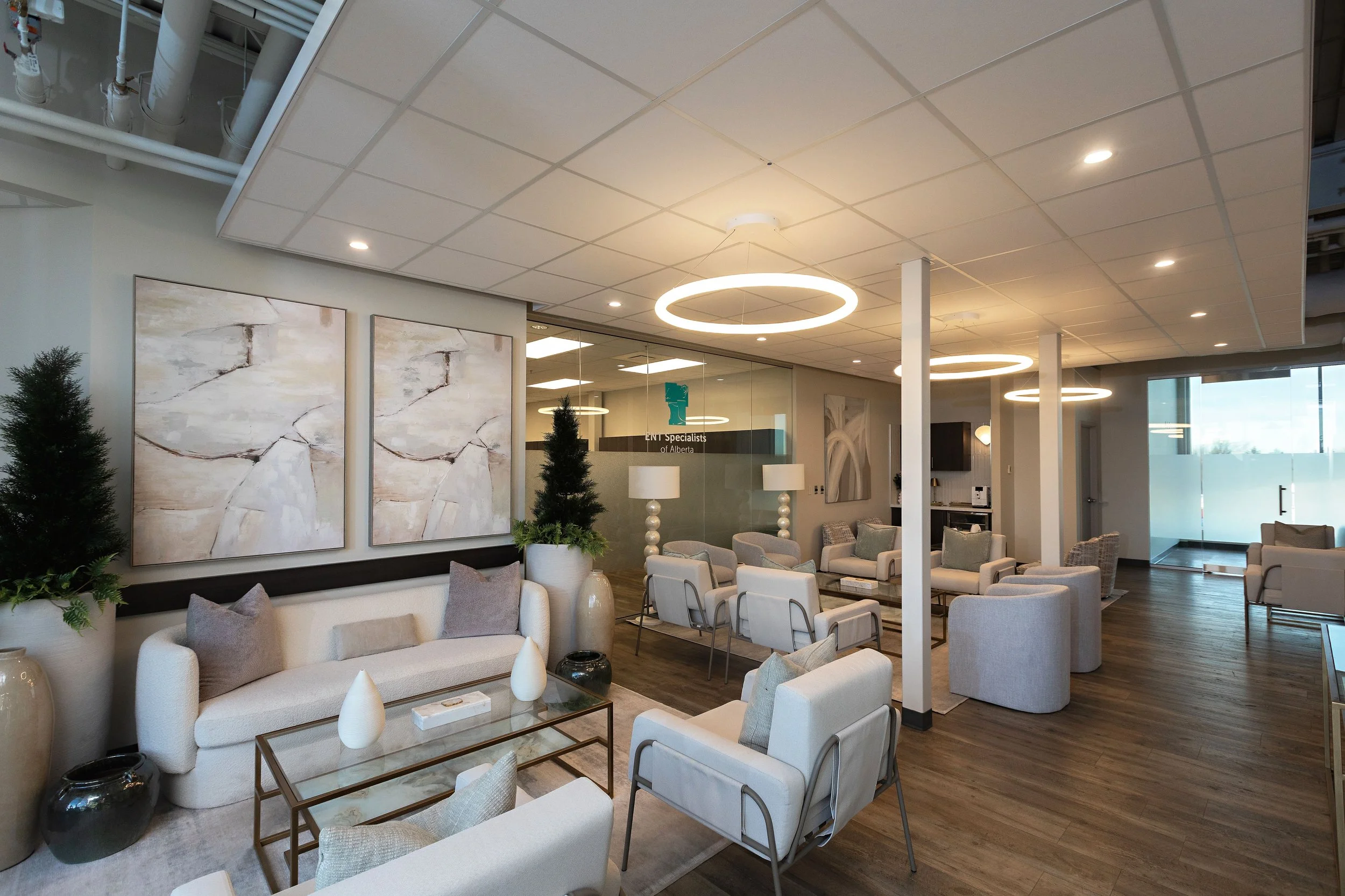 photo of a clinic waiting room with white sofas facing a glass coffee table and abstract paintings beneath circular light fixtures
