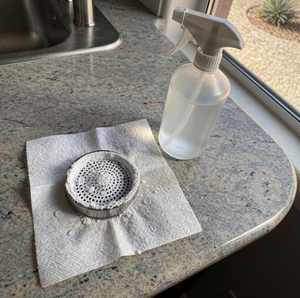 Kitchen sink drain strainer and spray bottle on a countertop.
