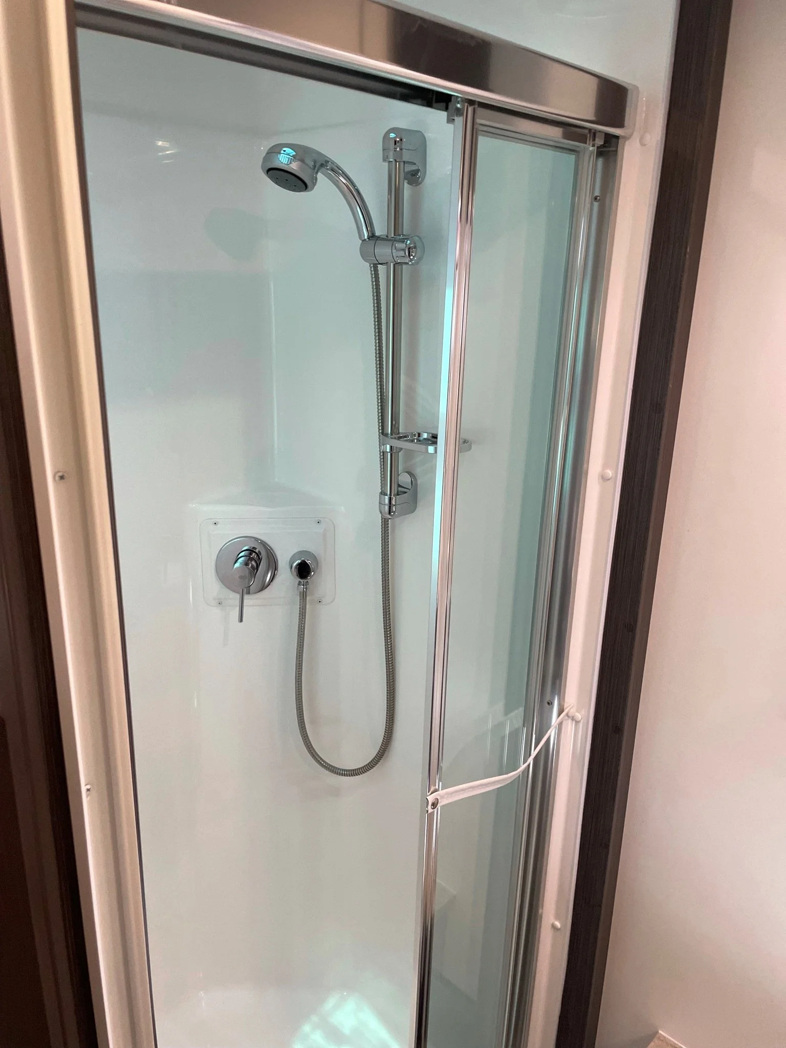 A modern enclosed shower with a glass door, handheld showerhead, and chrome fixtures.
