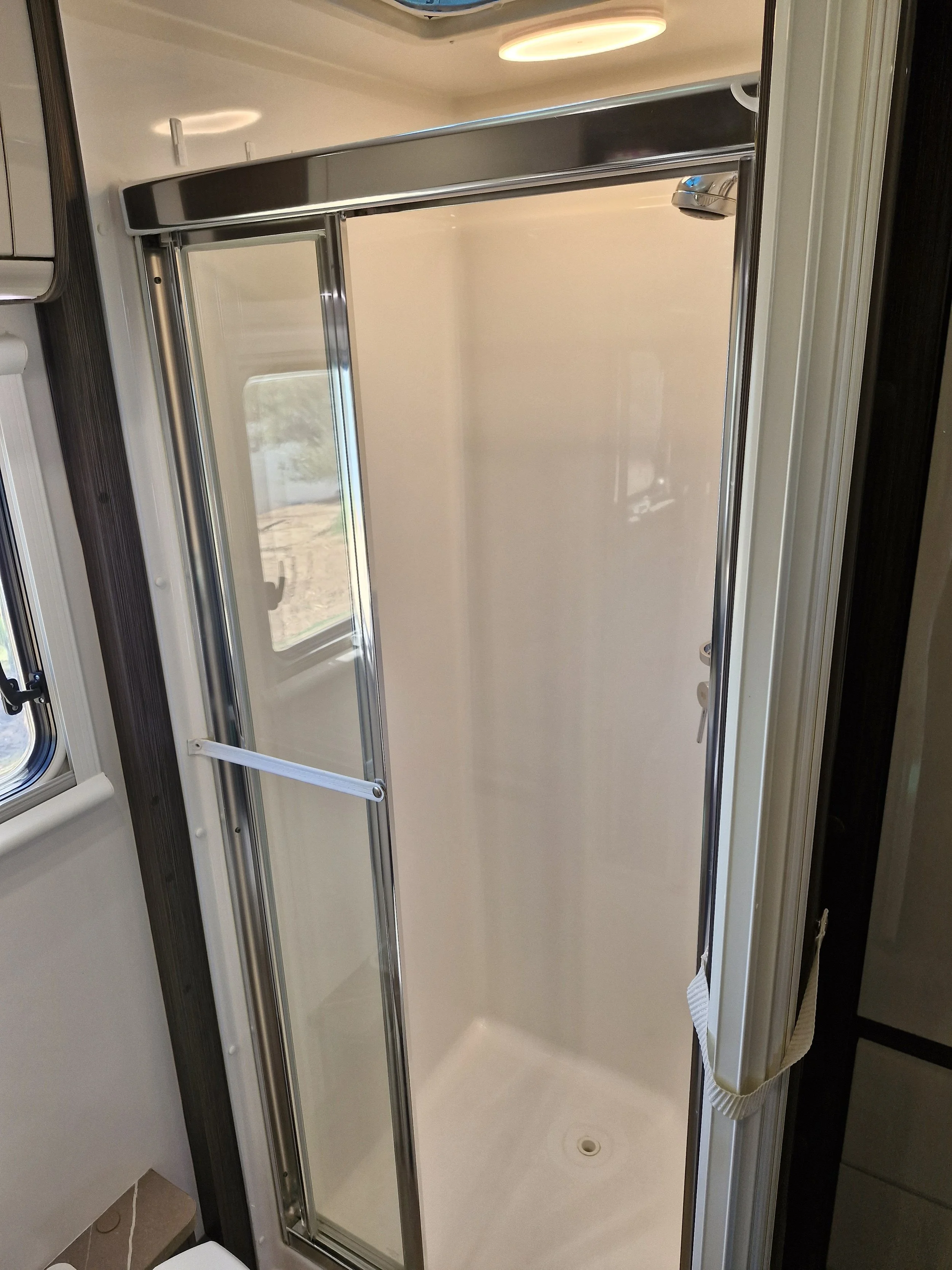 A shower with sliding glass doors, metal frame, and a small window to the left.