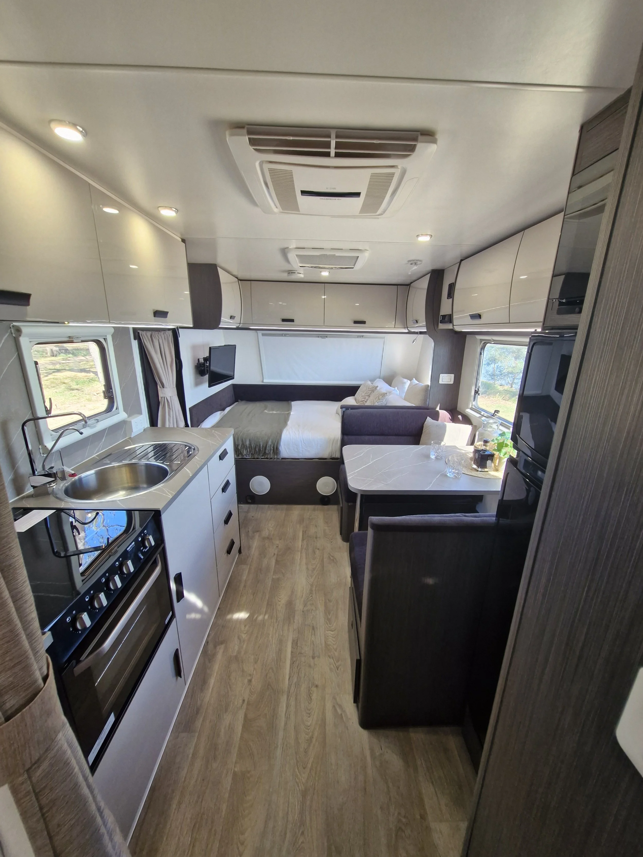 Interior of a modern camper or RV with kitchen area, bed, and seating.