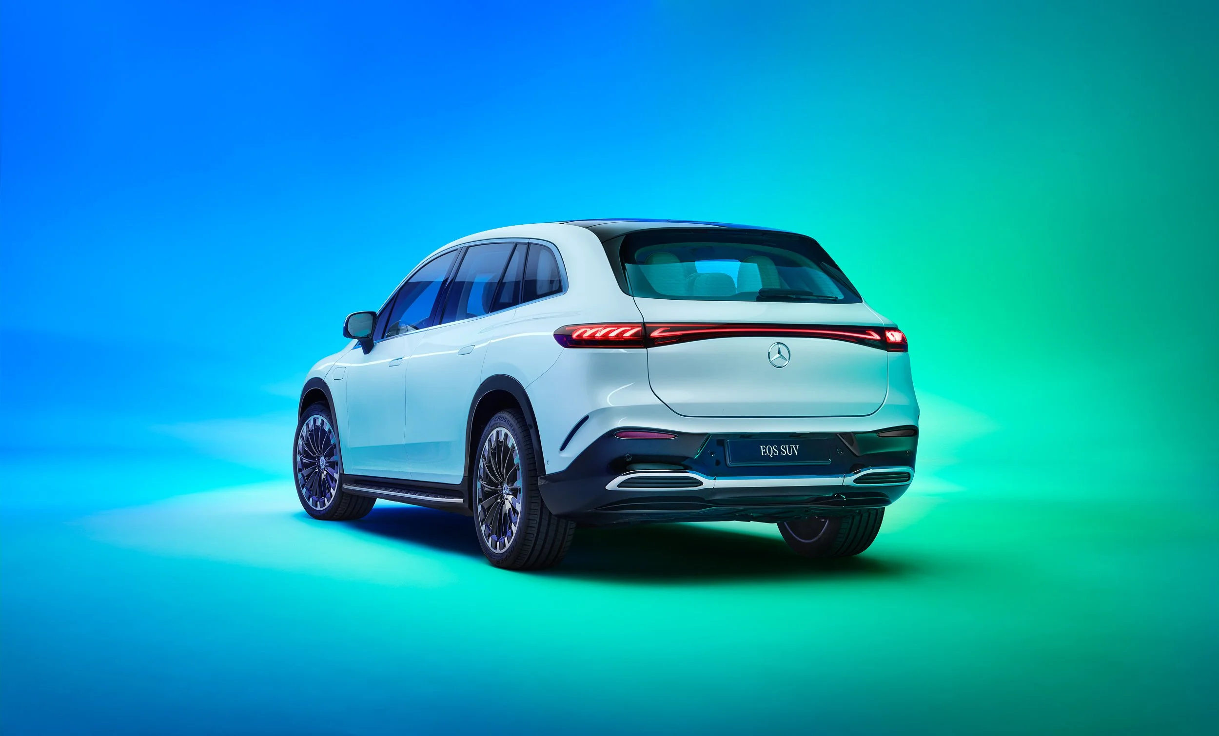 Rear view of a white Mercedes-Benz EQS SUV on a blue and green gradient background.