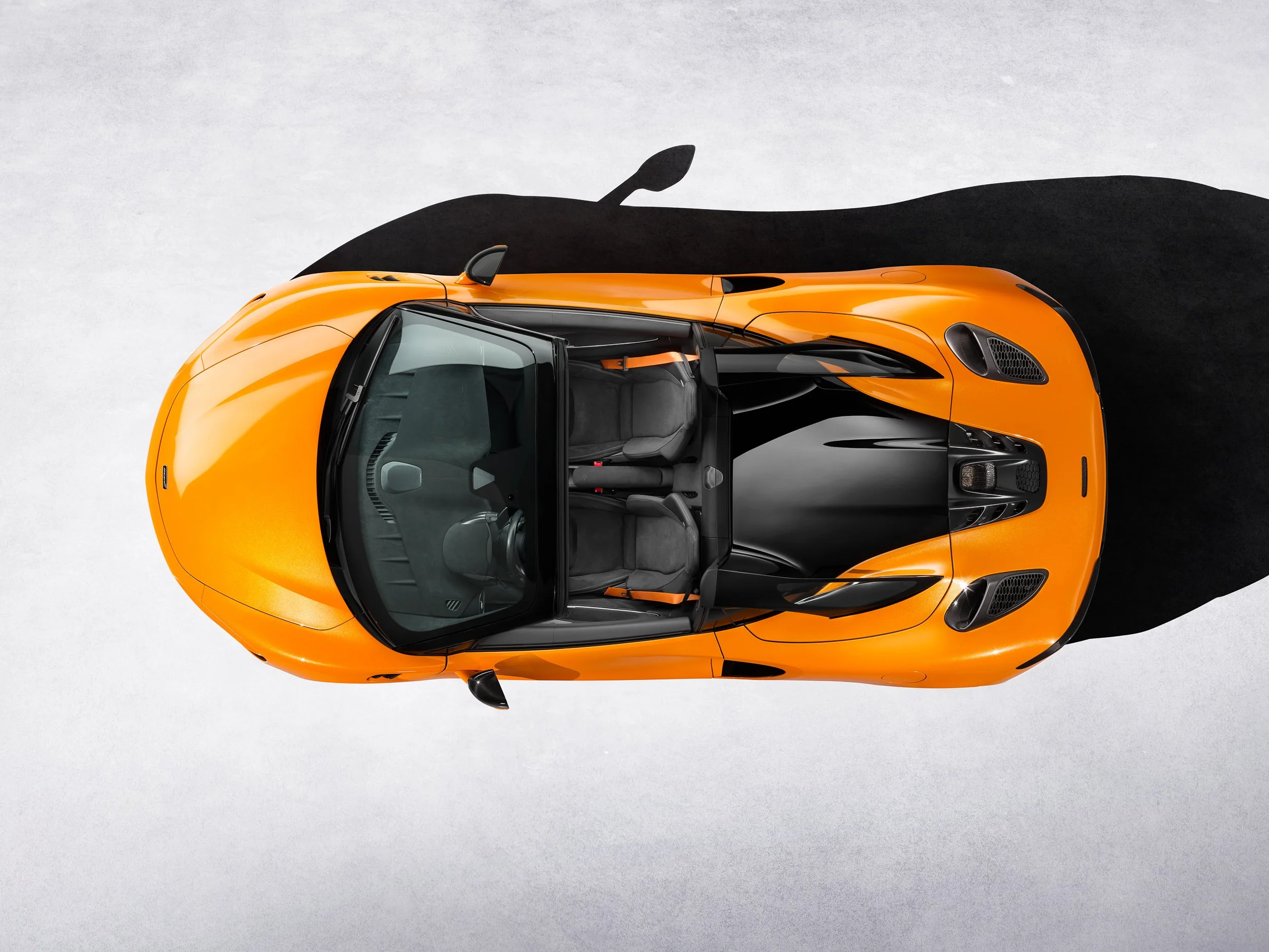 Orange sports car viewed from above with a pronounced shadow on a white background.