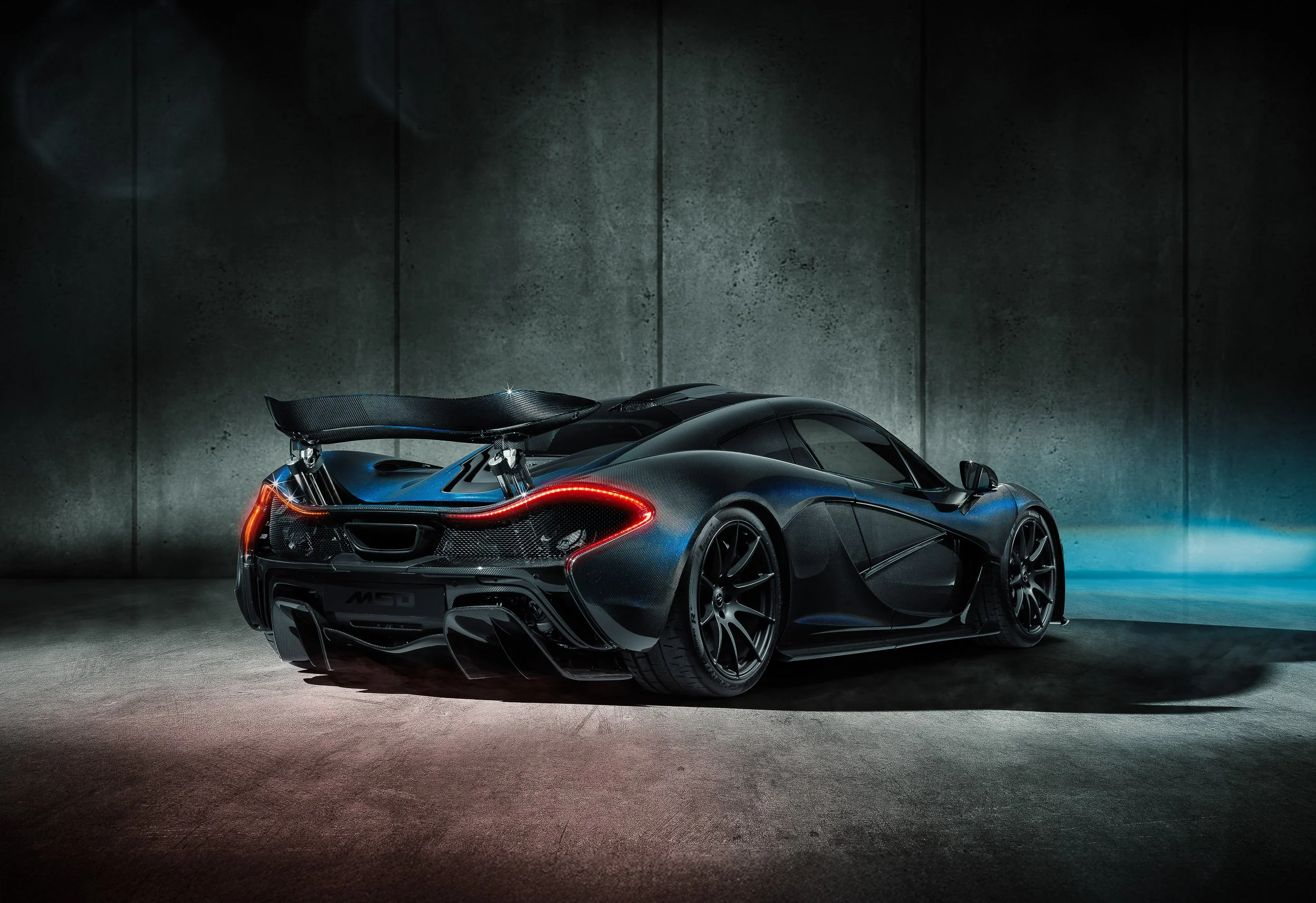 Rear view of a black McLaren P1 supercar in a dimly-lit, industrial-style studio.
