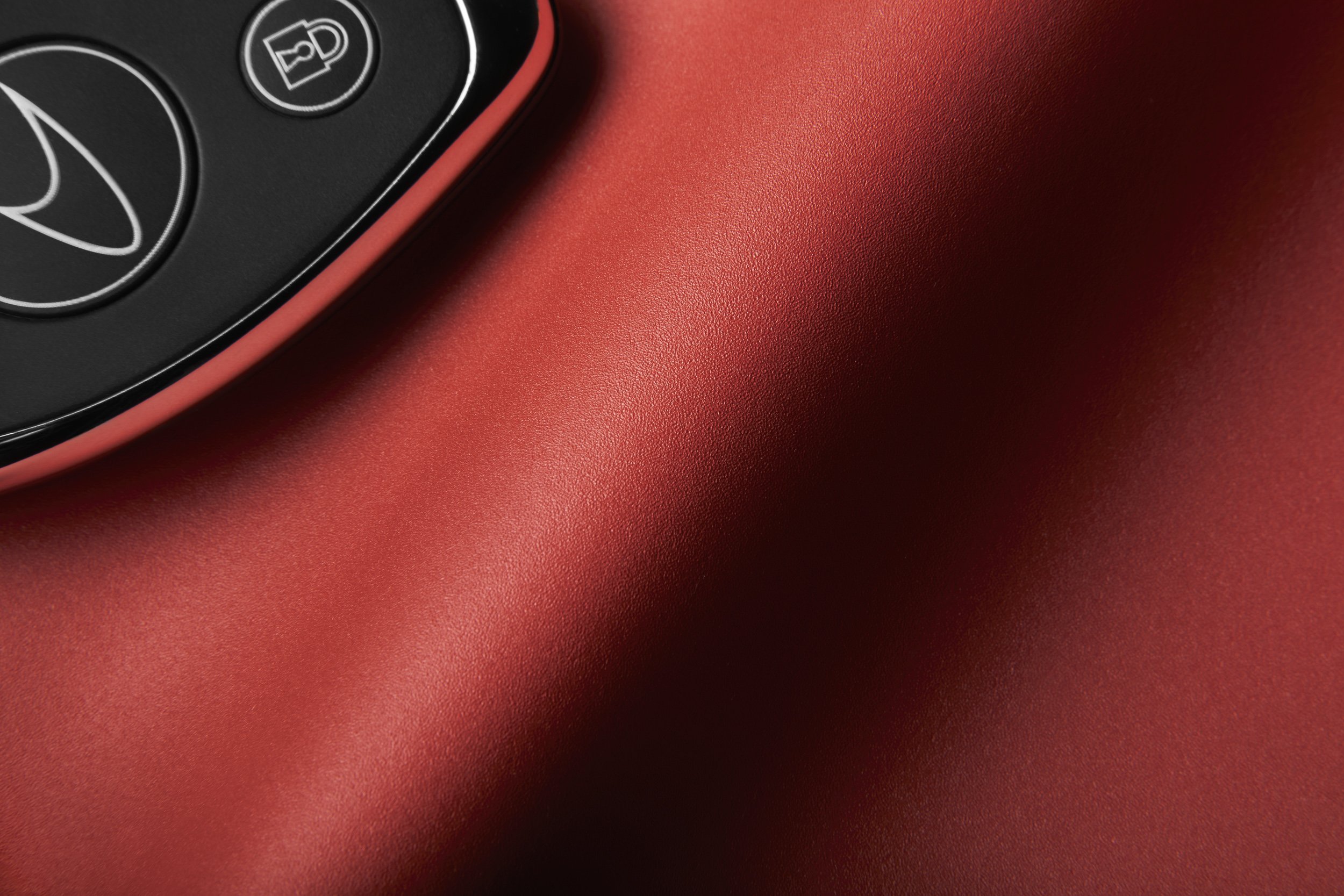 Close-up of a car key fob with a lock icon on a red surface.
