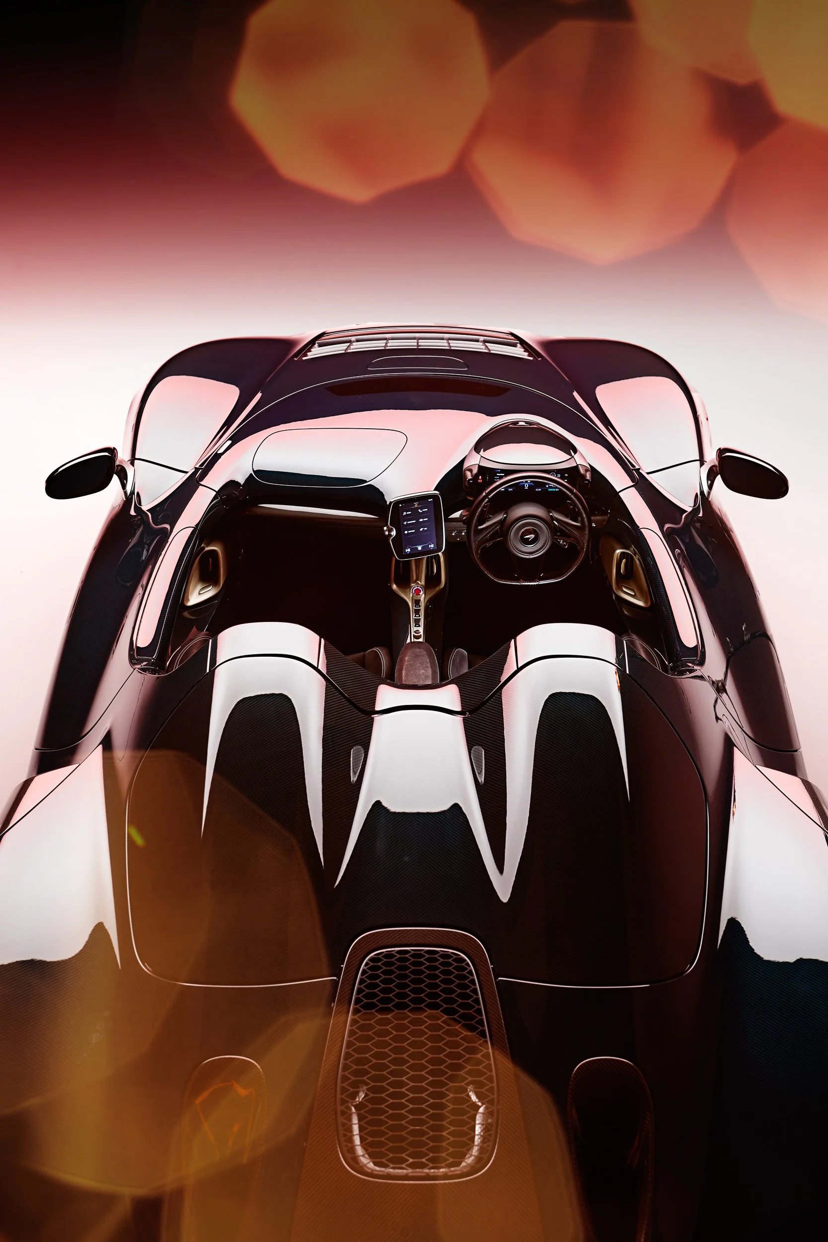 Top view of a sleek, black sports car interior with a modern dashboard, steering wheel, and central touchscreen display, set against a blurred background with soft lighting effects.