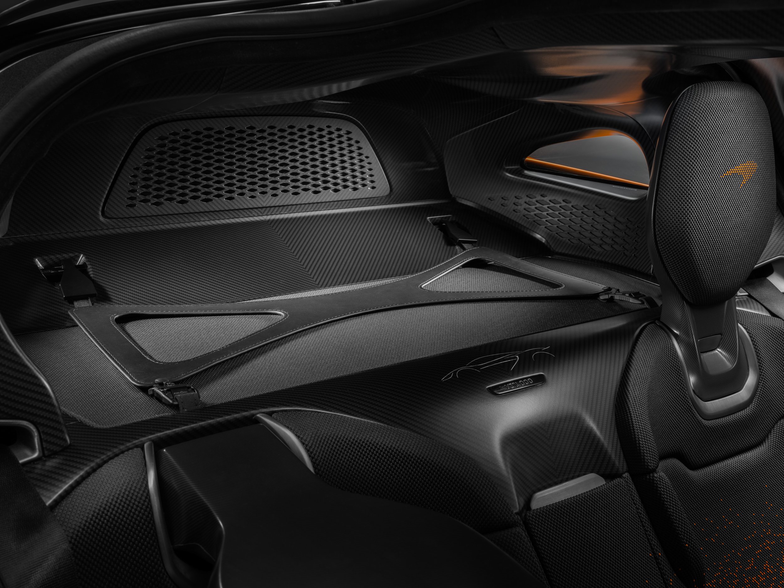 Interior of a luxury sports car with a carbon fiber finish, featuring a sleek seat design and a visible logo on the seat's headrest.