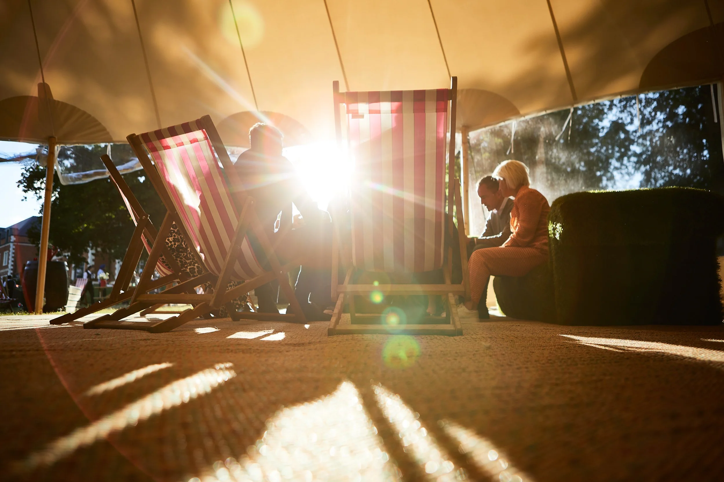People sitting on deck chairs under a canopy with sunlight streaming through, creating shadows and a warm ambiance.
