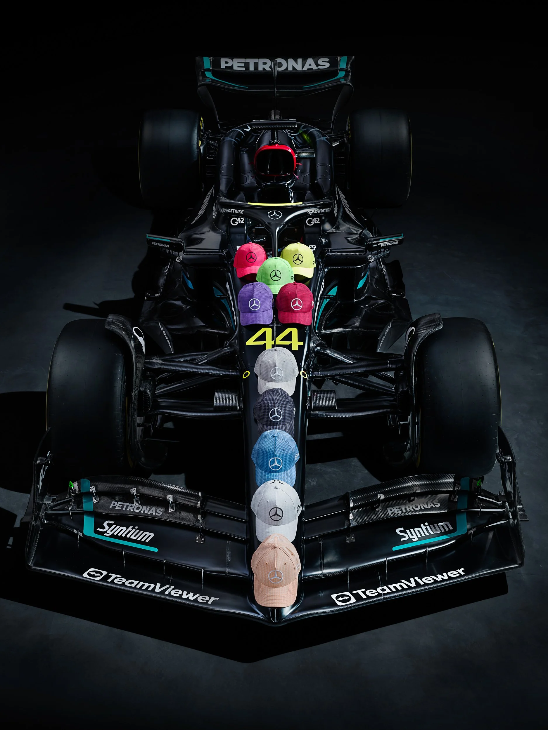 Black Formula 1 car with colorful Mercedes-Benz caps arranged on the car's nose, featuring branding from Petronas, Syntium, and TeamViewer.
