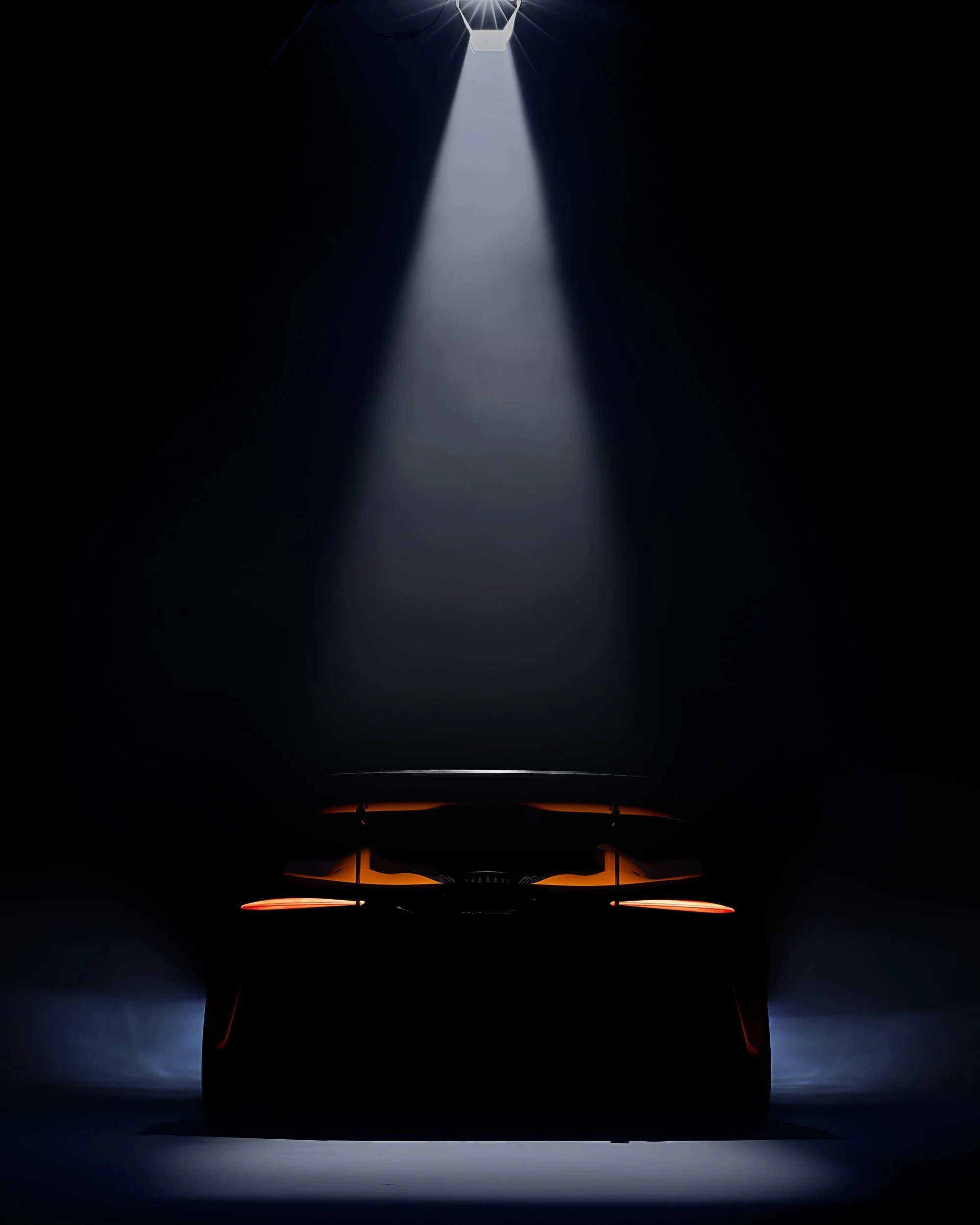 Silhouette of a car under spotlight in a dark environment; rear view.
