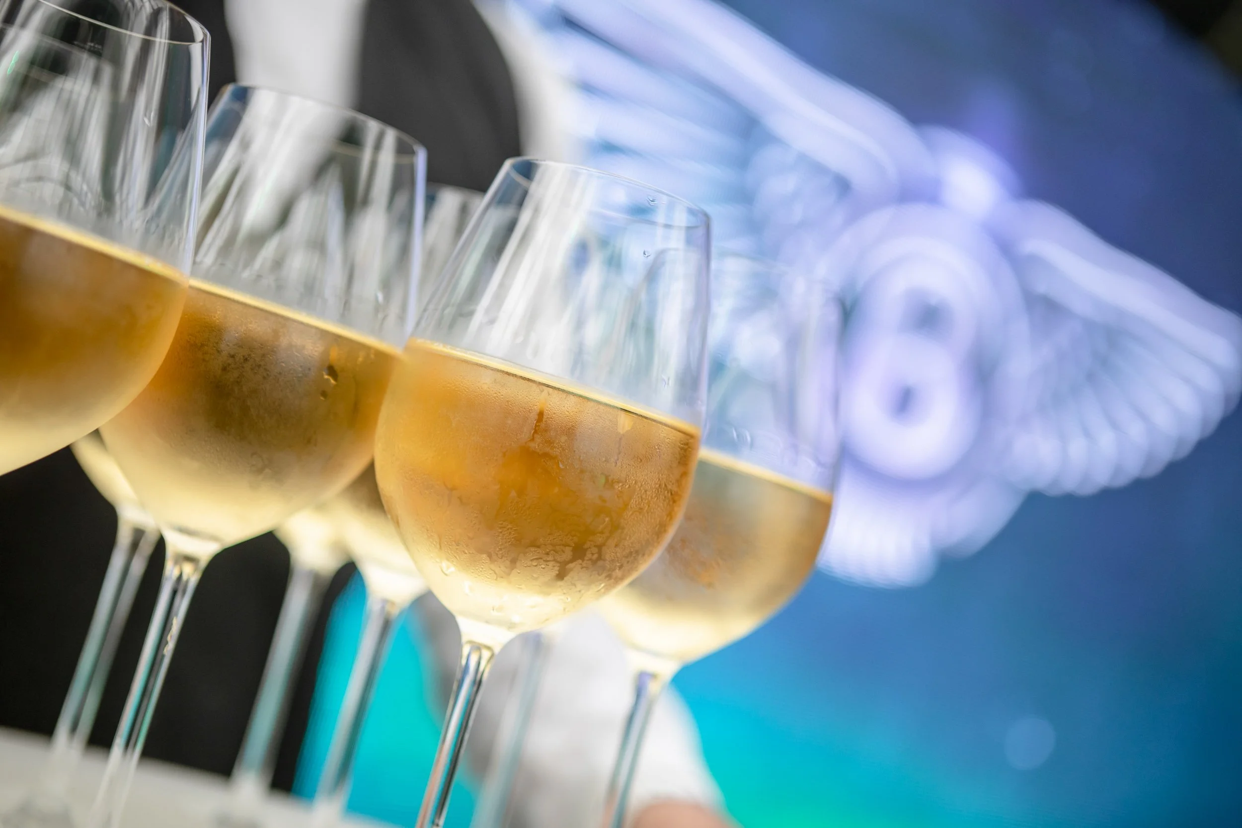 Glasses of champagne on a tray with a blurred background featuring a stylized logo.