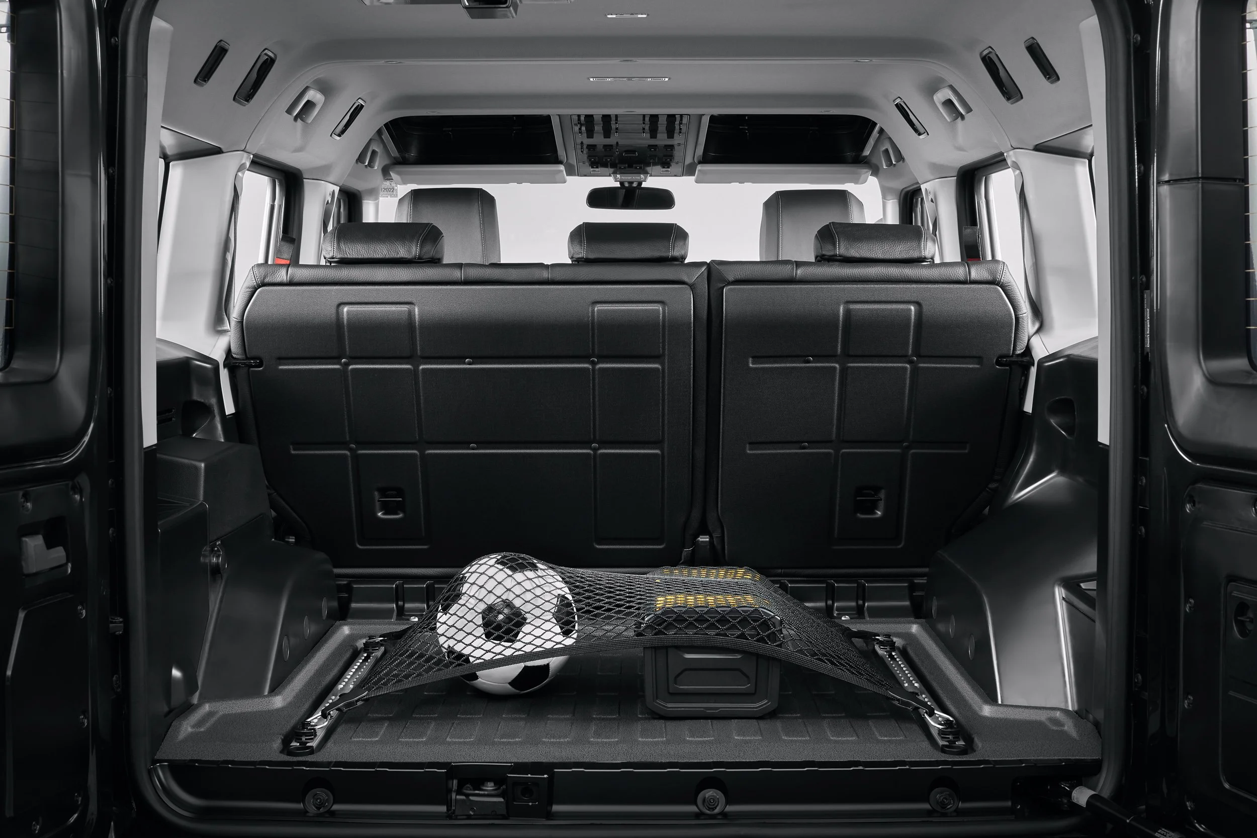 Interior of a vehicle with rear seats folded, cargo net holding a soccer ball and containers in the trunk.