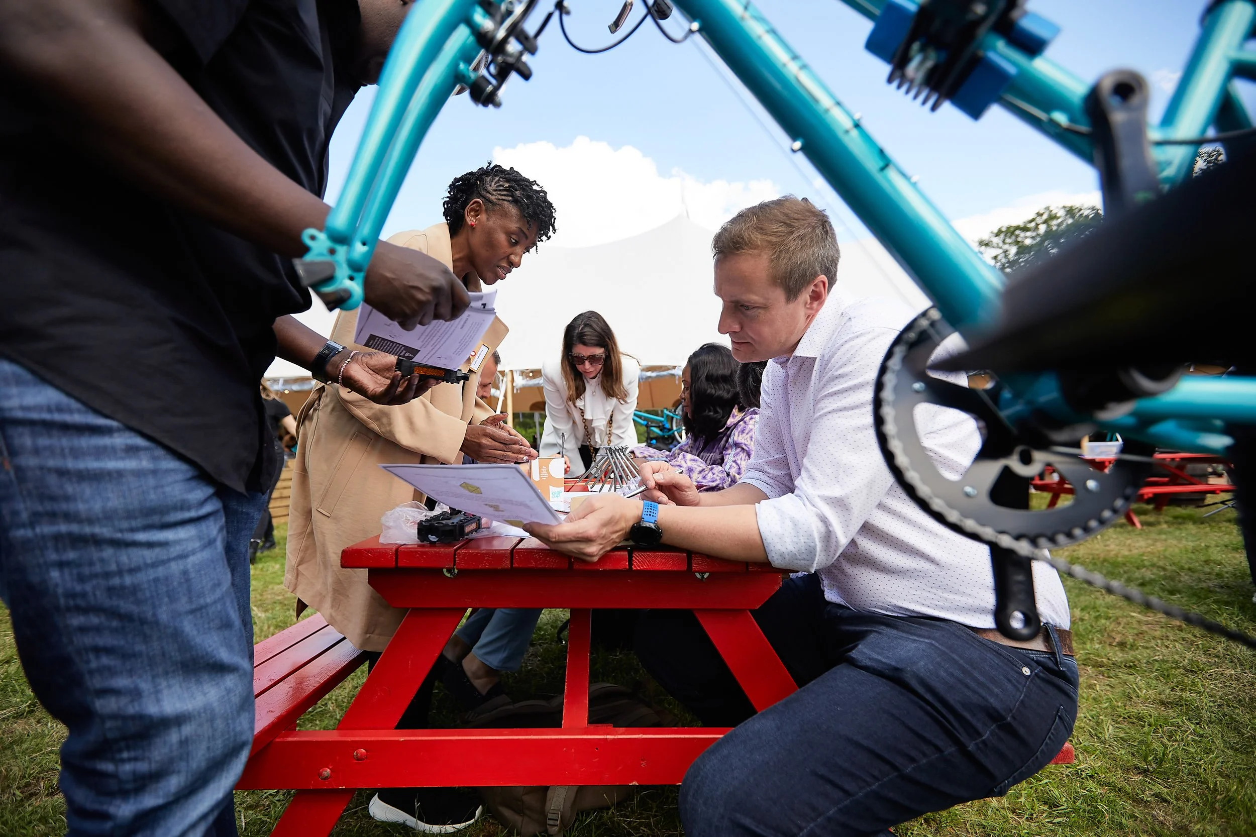 People gathered around a red picnic table with a bicycle in the foreground.