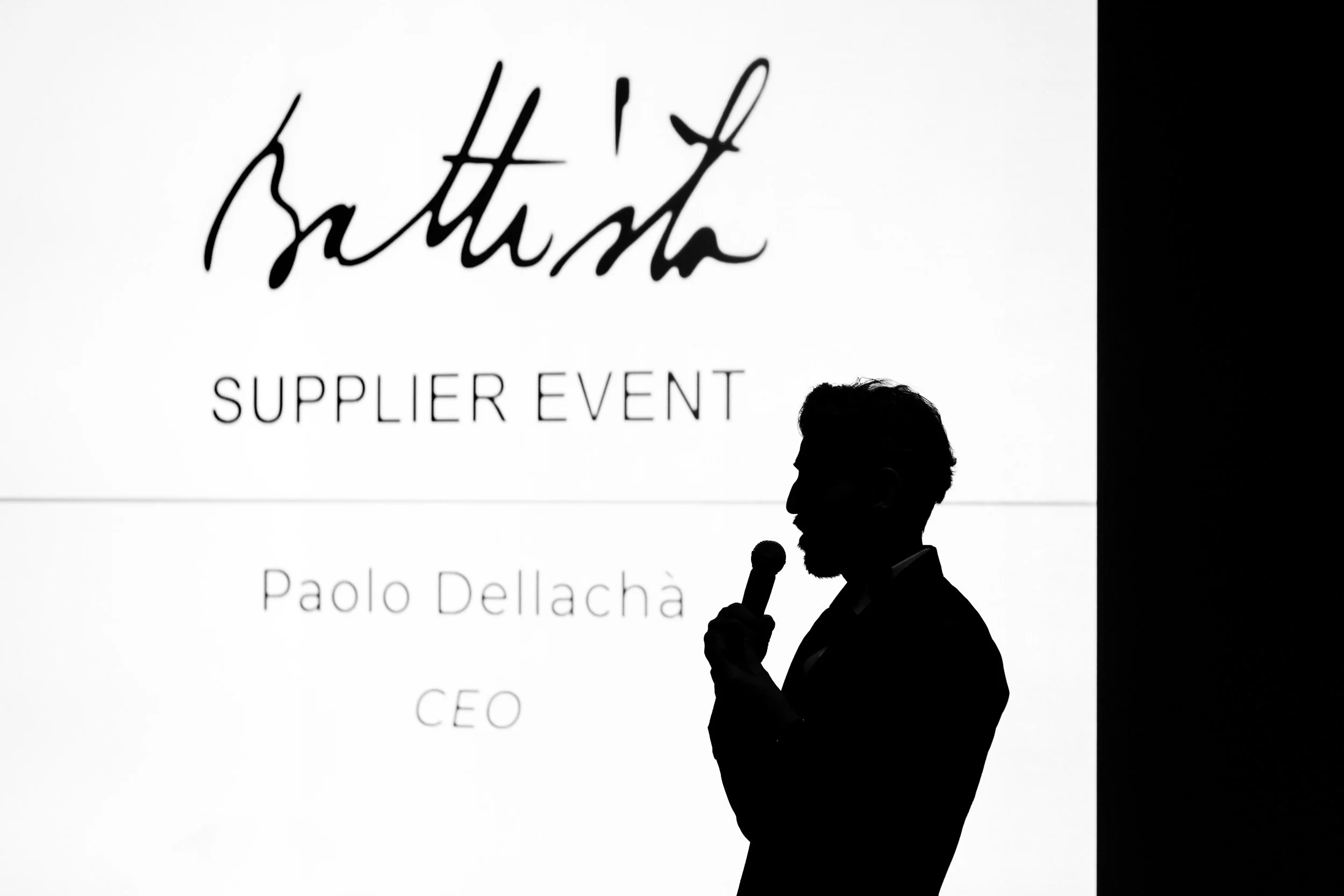 Silhouette of a man speaking into a microphone at a Battista Supplier Event.