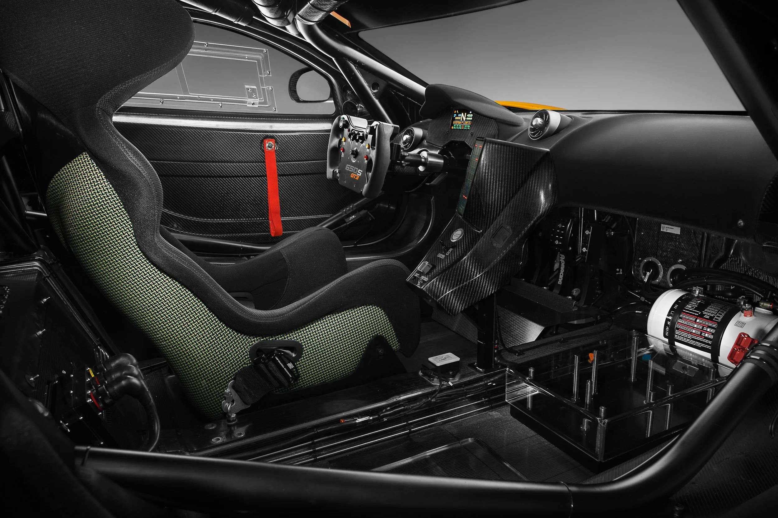 Interior of a race car featuring a racing seat, steering wheel with controls, fire extinguisher, and carbon fiber elements.