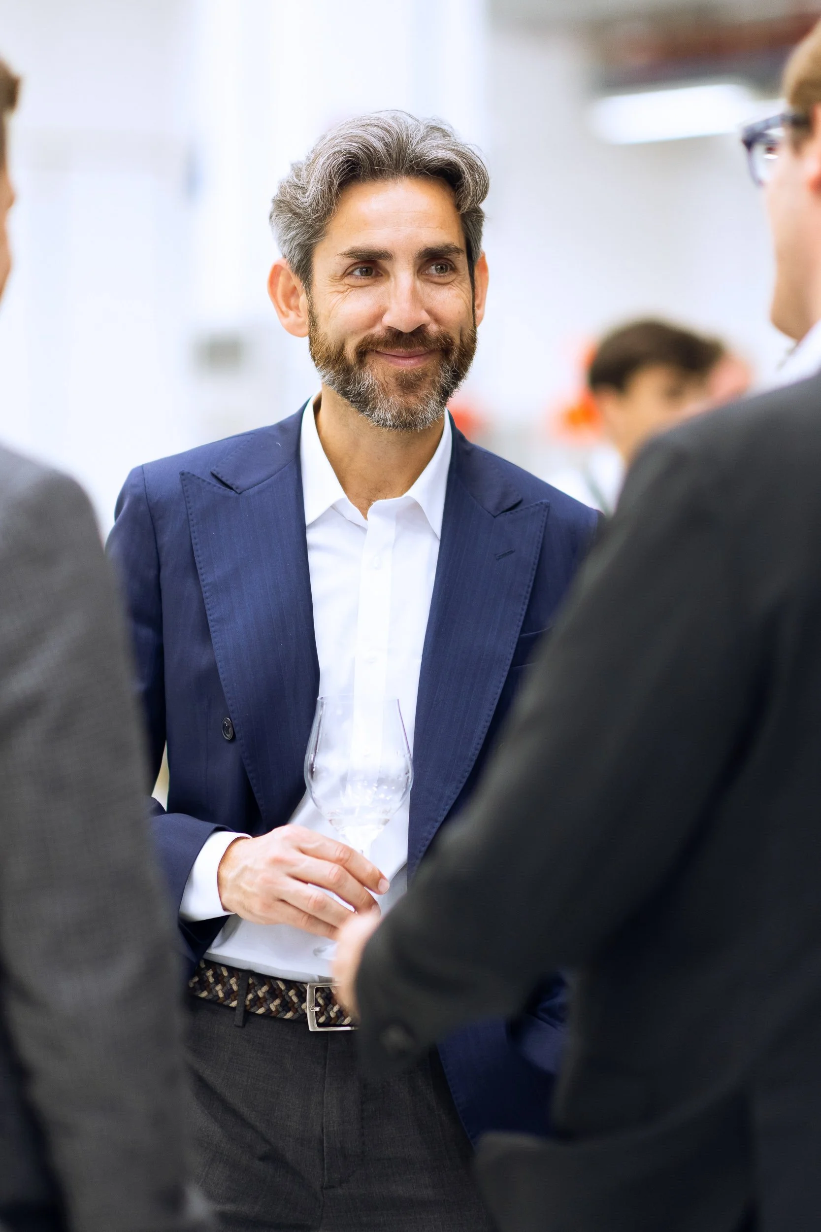 Man in a suit holding a wine glass, engaged in conversation at a social event.