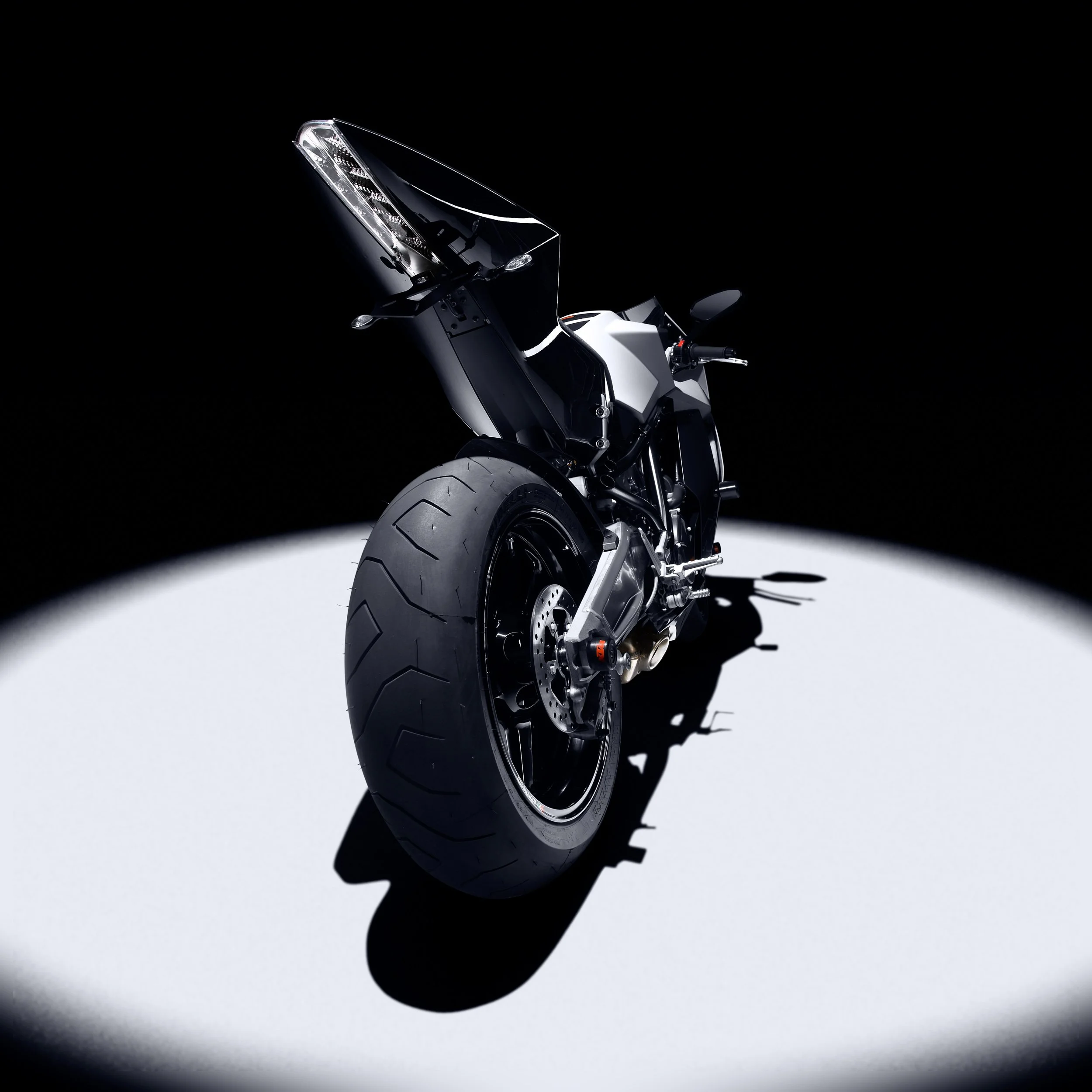 Rear view of a modern high-performance motorcycle with a spotlight on its rear tire and tail section, against a dark background.