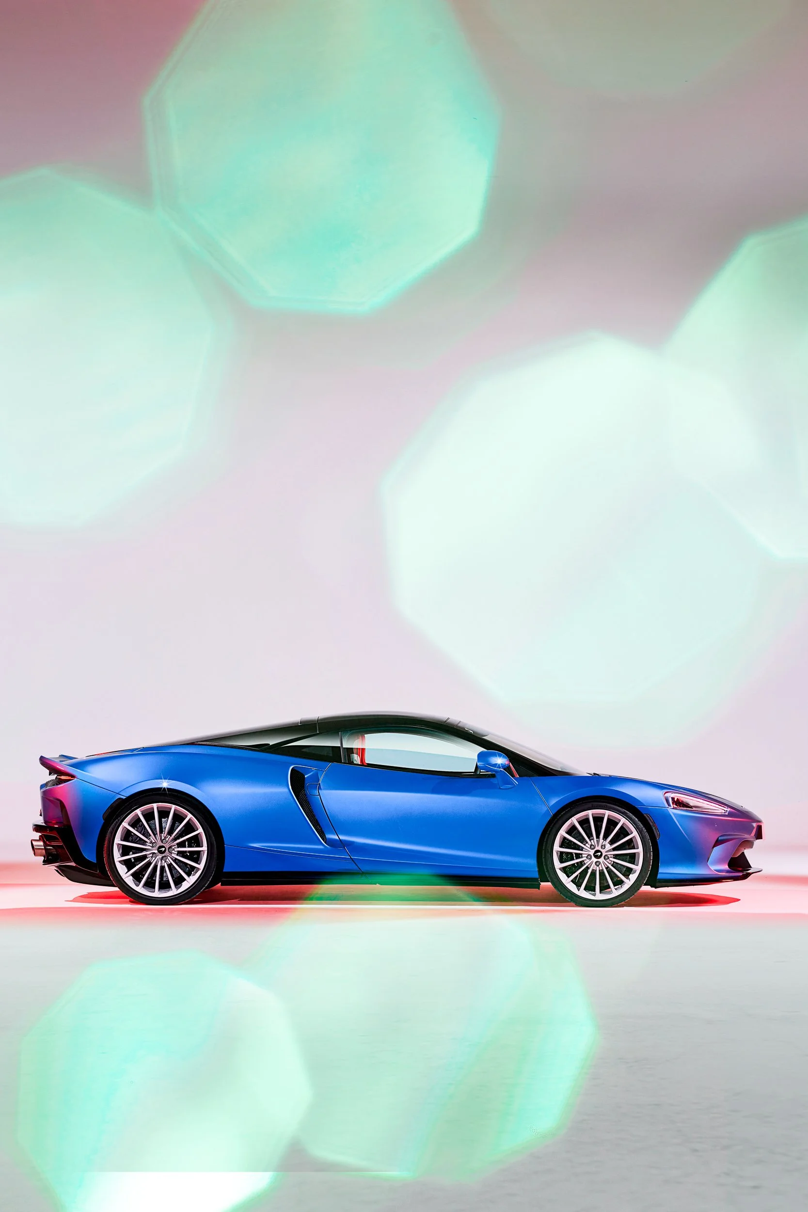 Blue sports car with a sleek design and alloy wheels in a studio setting, surrounded by abstract green bokeh lights.