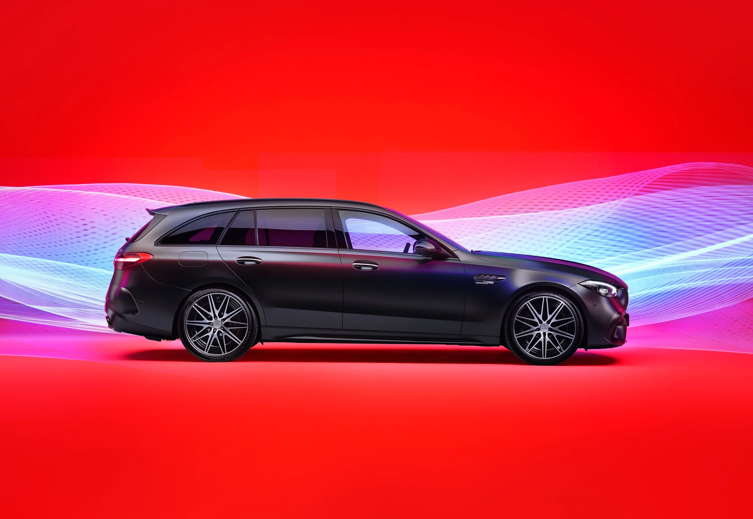 Black luxury station wagon against vibrant red background with dynamic light trails.