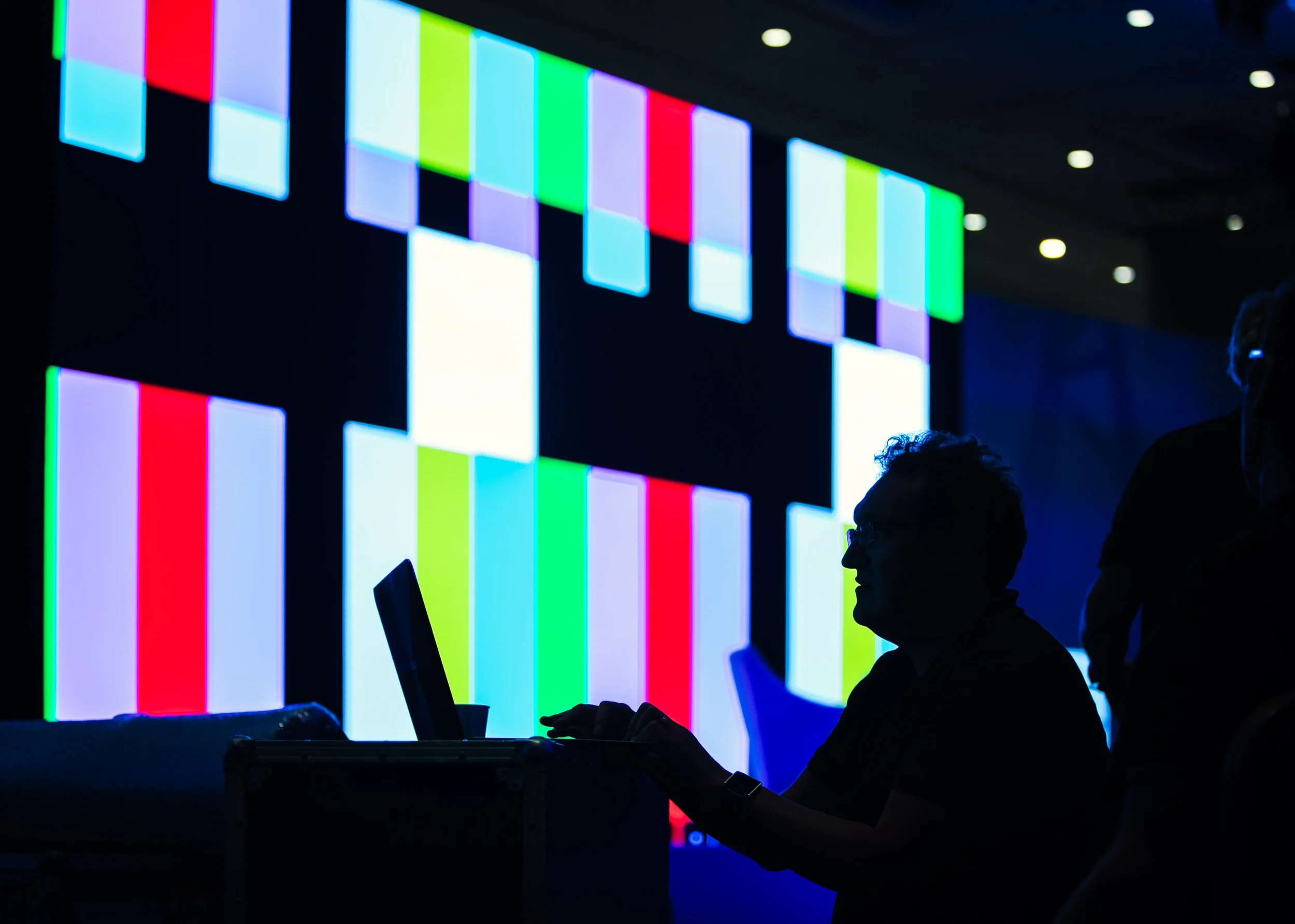 Silhouette of a person using a laptop in front of a colorful LED screen displaying abstract patterns.