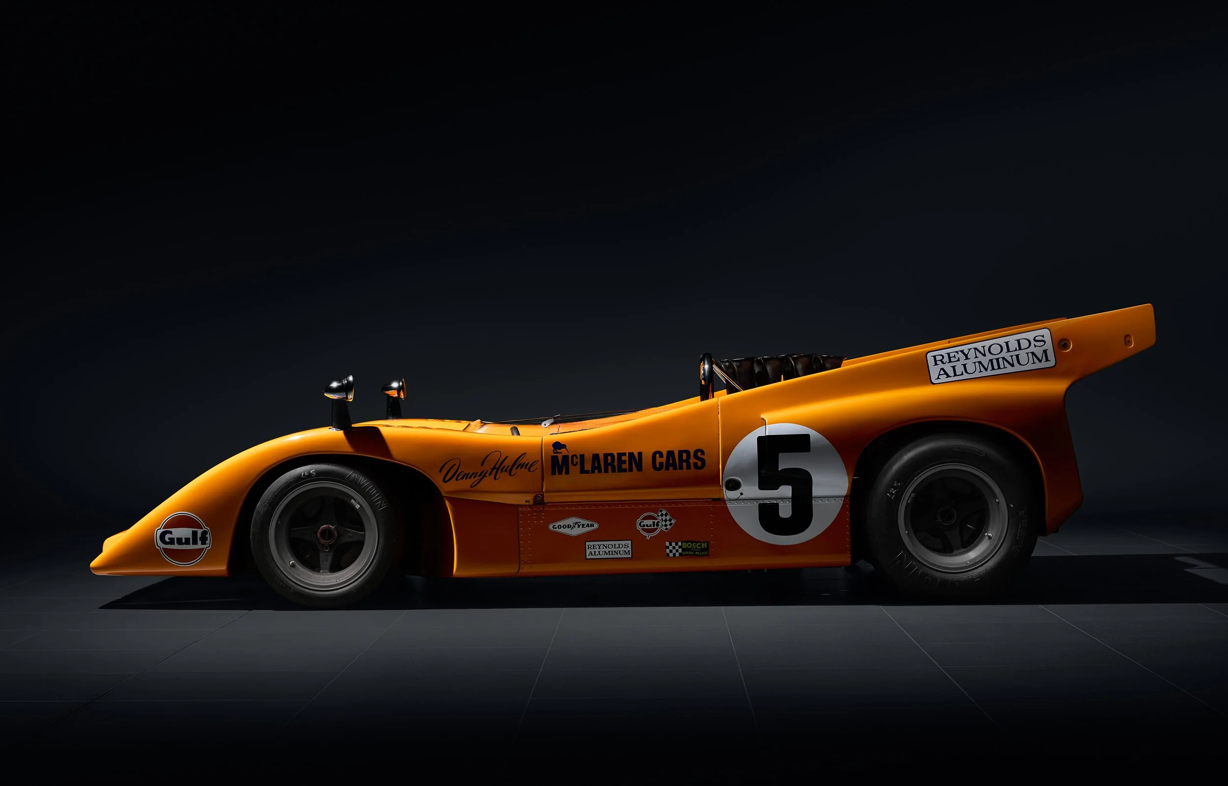 Orange vintage McLaren race car with number 5 and various sponsor logos on a dark background.