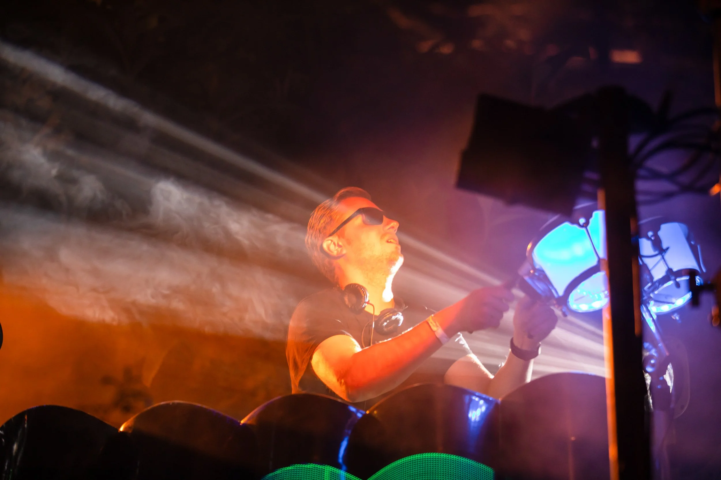 DJ performing with light effects, wearing headphones and sunglasses