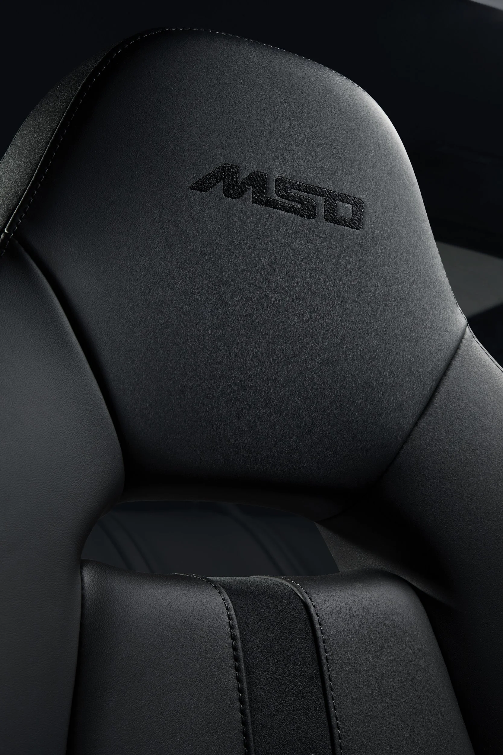 Close-up of a black leather car seat with "MSO" logo embroidered on the headrest.